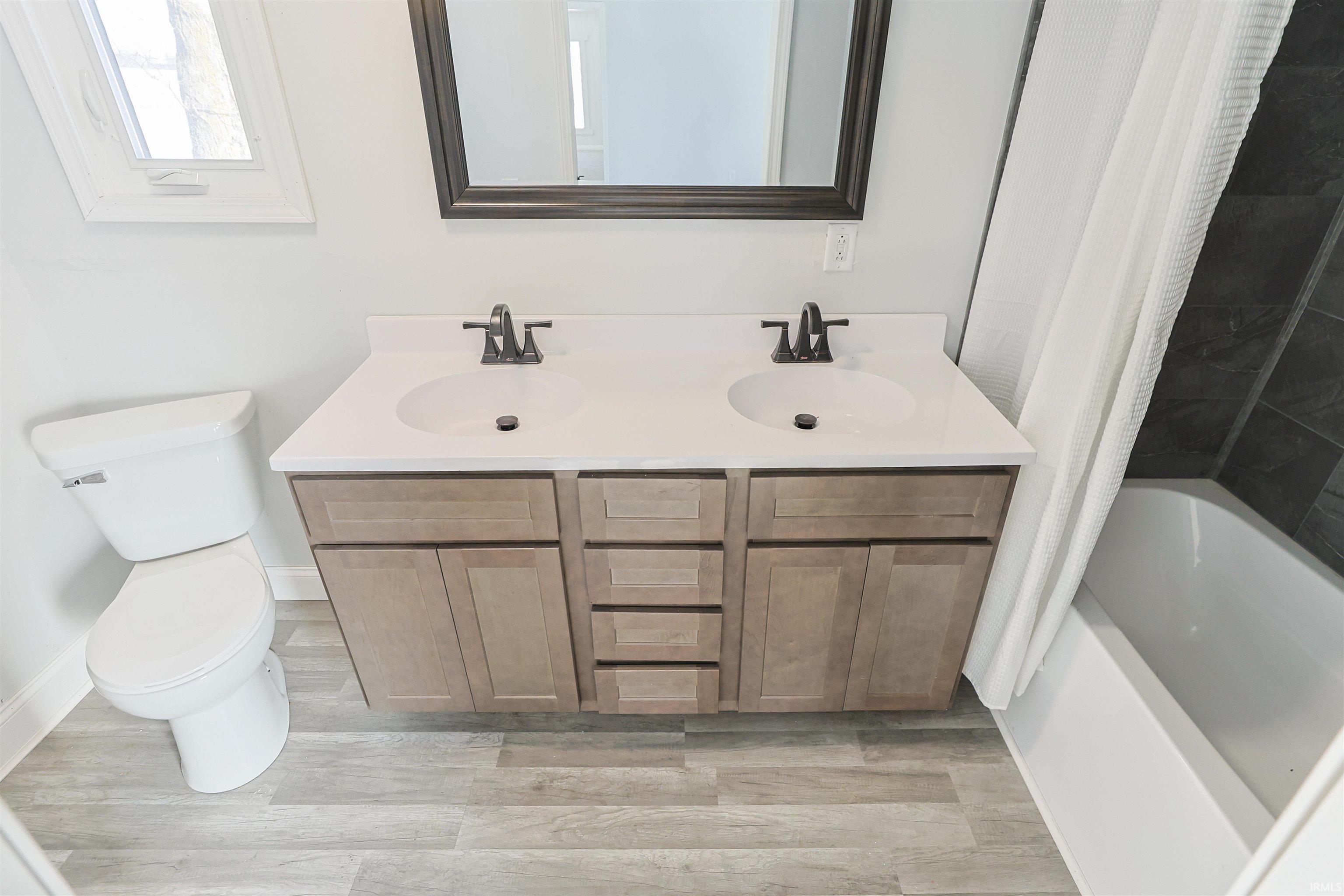 Bathroom with double vanity, shower / bath combo, and light wood finished floors