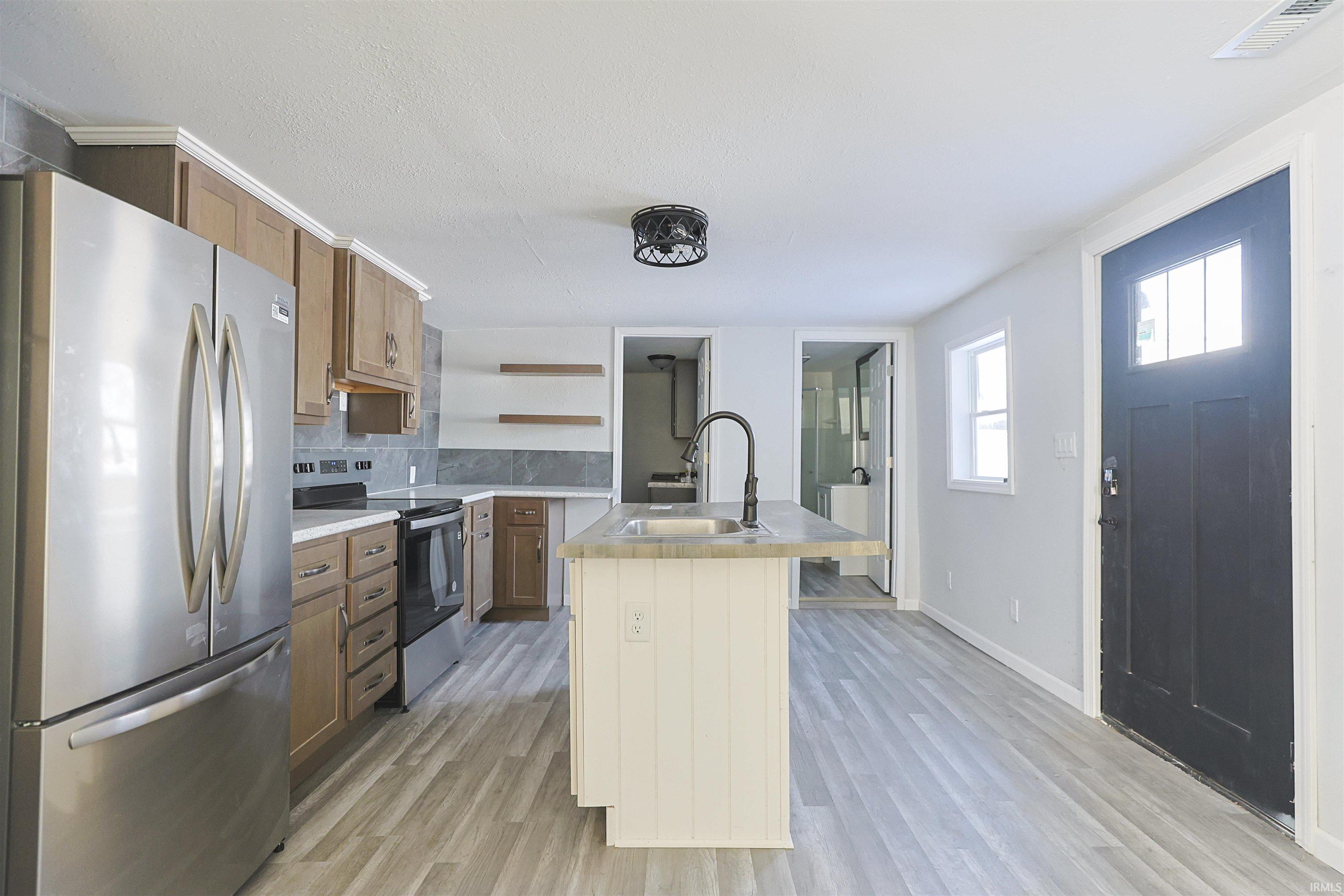 Kitchen with light countertops, appliances with stainless steel finishes, decorative backsplash, a center island with sink, and open shelves