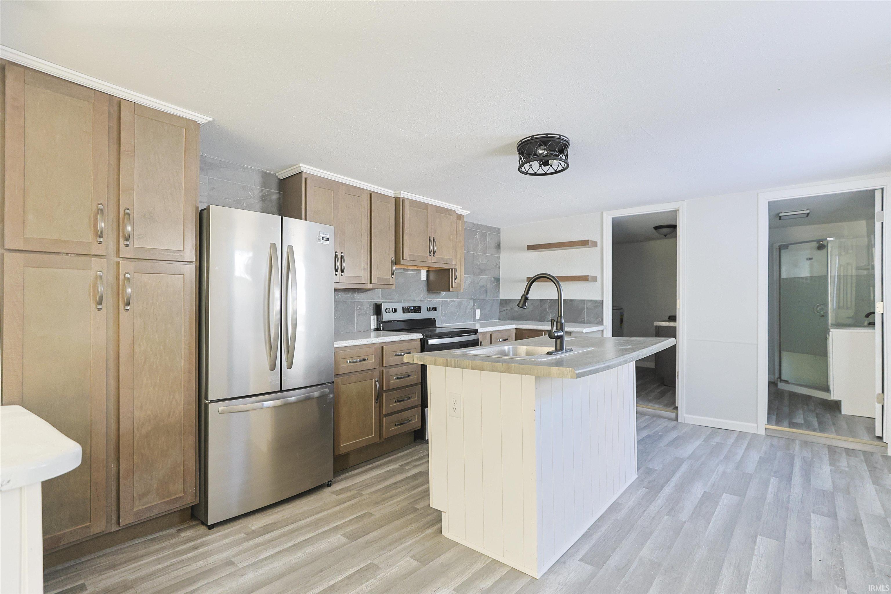 Kitchen featuring light countertops, appliances with stainless steel finishes, light wood-style flooring, and open shelves