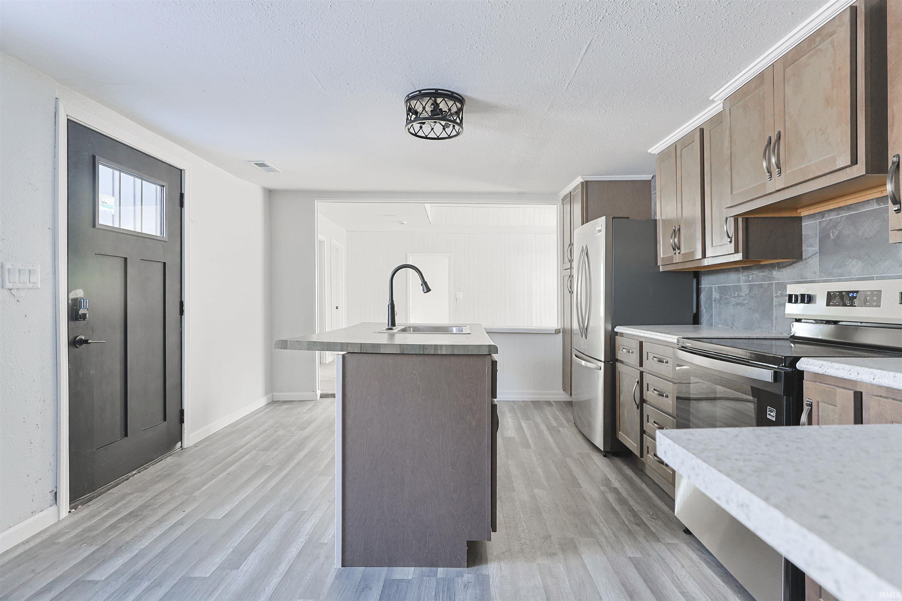 Kitchen featuring appliances with stainless steel finishes, a kitchen island with sink, light countertops, tasteful backsplash, and a textured ceiling