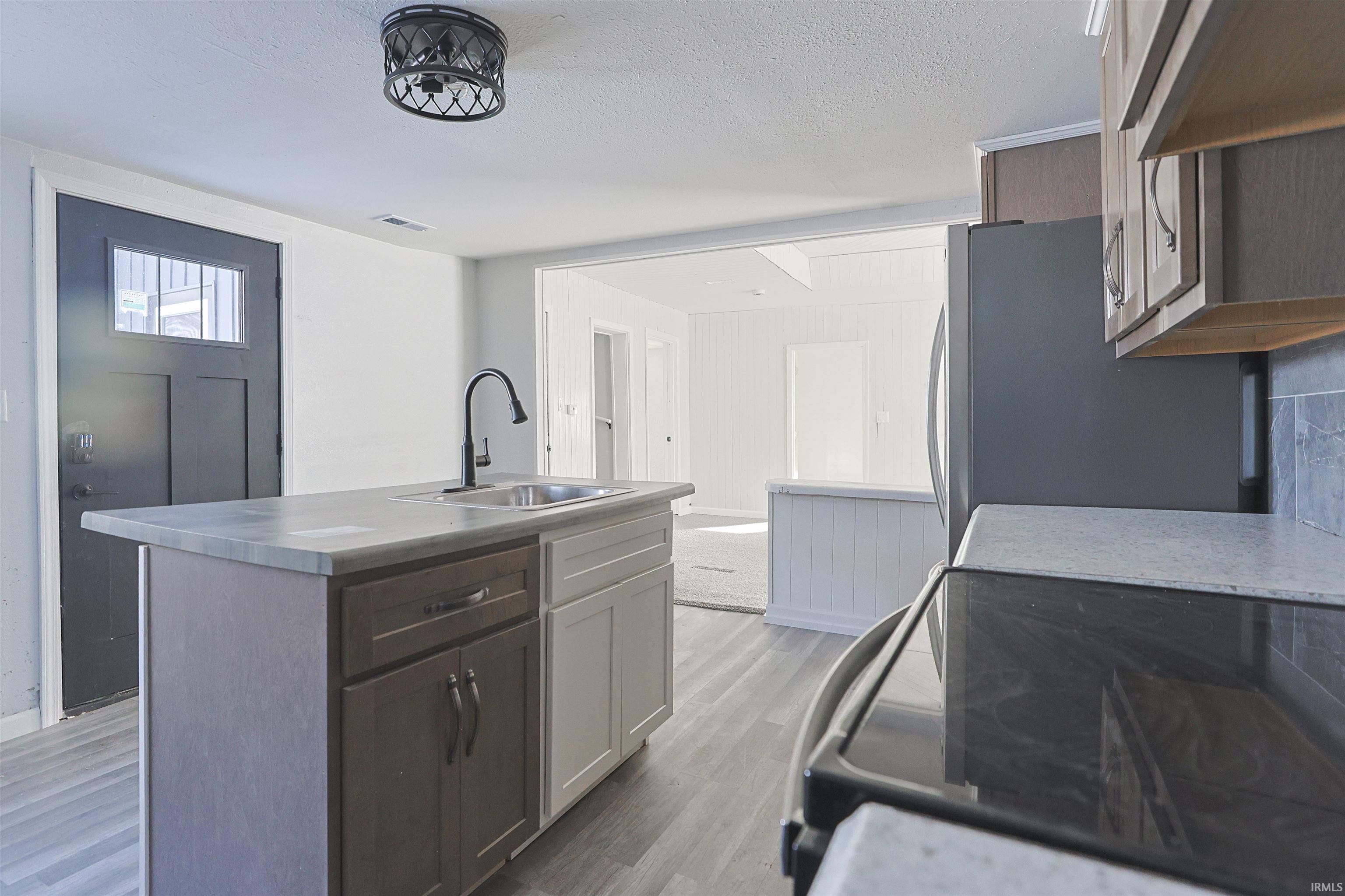 Kitchen with a kitchen island with sink, light wood-style floors, black electric range, freestanding refrigerator, and a textured ceiling