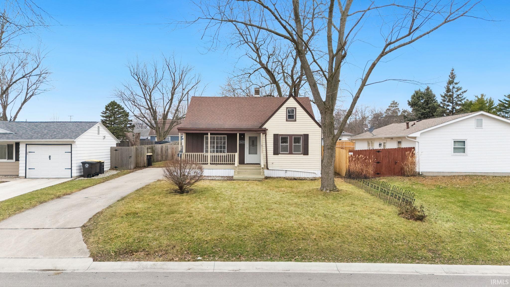 View of front facade featuring covered porch, driveway, roof with shingles, and a gate