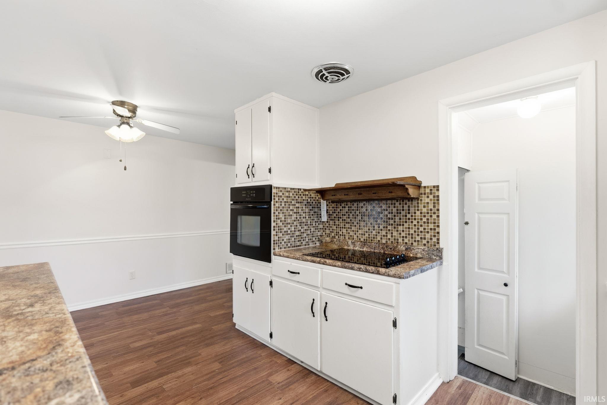 Kitchen with white cabinets, dark wood-type flooring, black appliances, ceiling fan, and tasteful backsplash