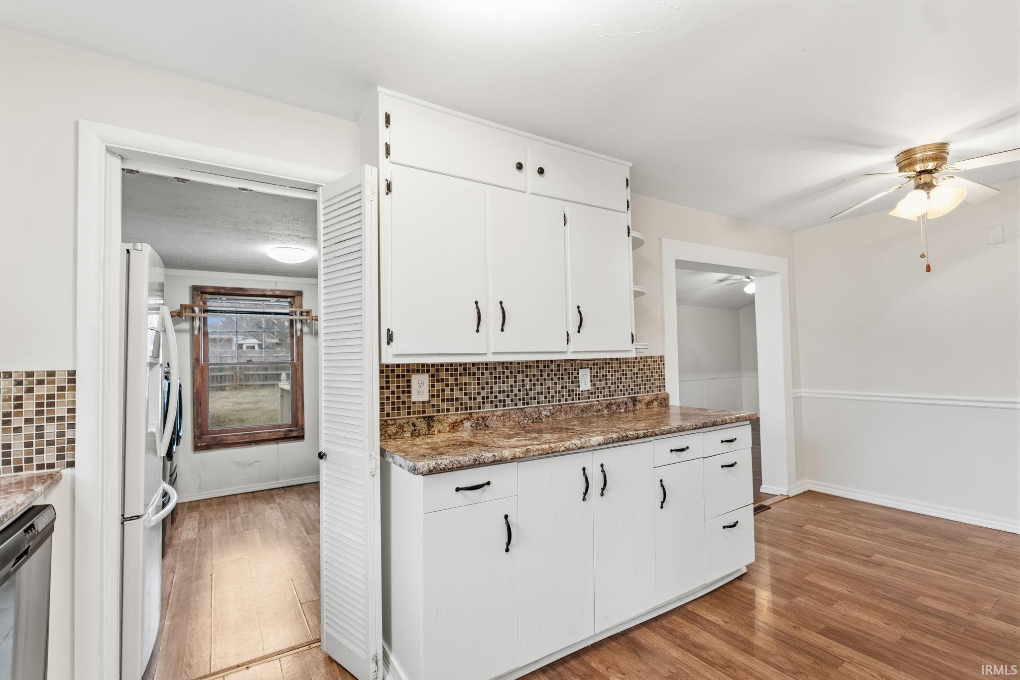Kitchen with tasteful backsplash, light wood-style floors, ceiling fan, and white cabinets