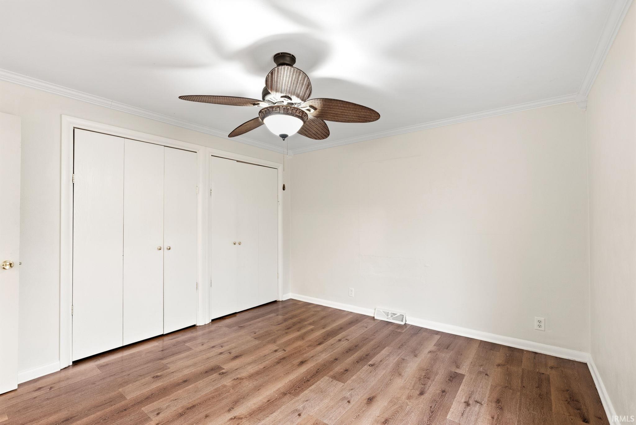 Unfurnished bedroom featuring multiple closets, light wood finished floors, ornamental molding, and ceiling fan