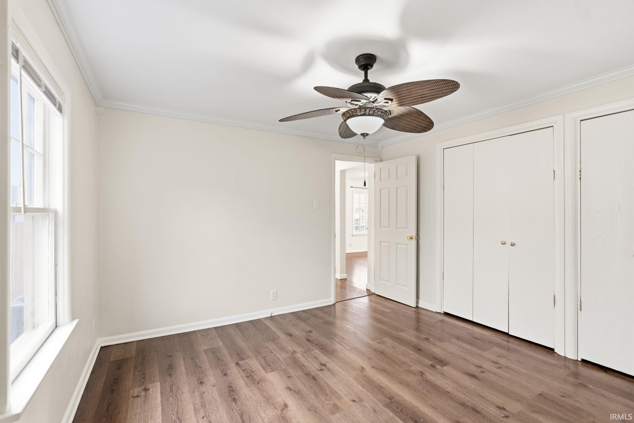 Unfurnished bedroom with crown molding, wood finished floors, ceiling fan, and multiple closets