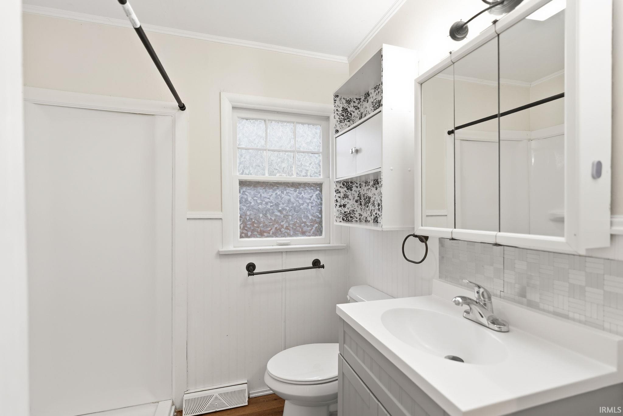 Bathroom featuring vanity, wainscoting, a shower, crown molding, and dark wood-type flooring