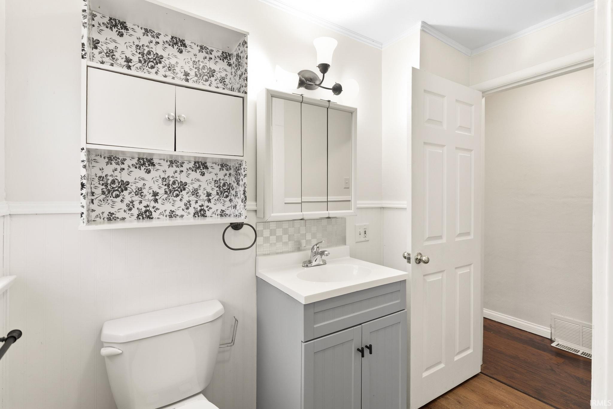 Half bath with vanity, crown molding, dark wood-style flooring, and backsplash