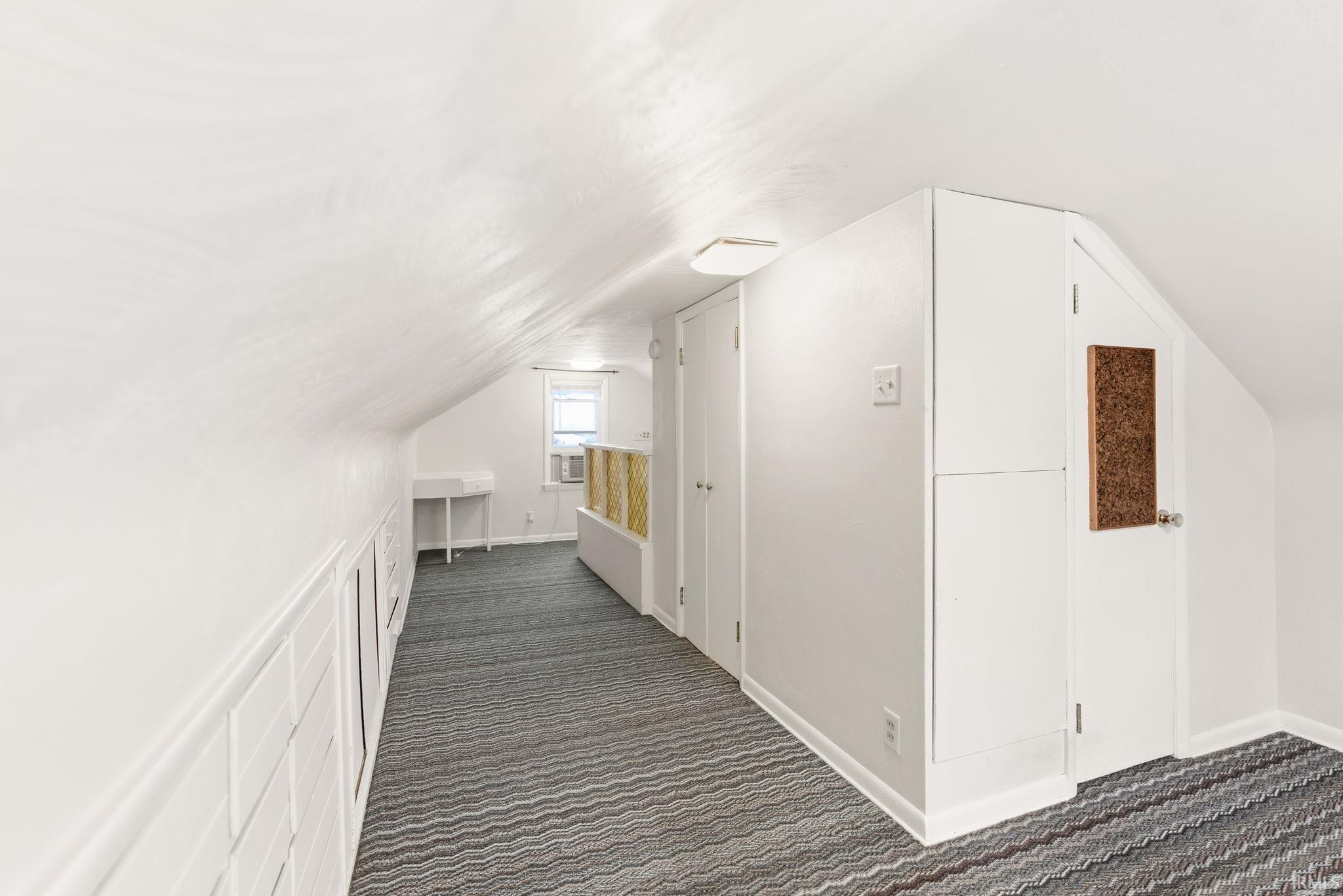 Bonus room with dark colored carpet and vaulted ceiling