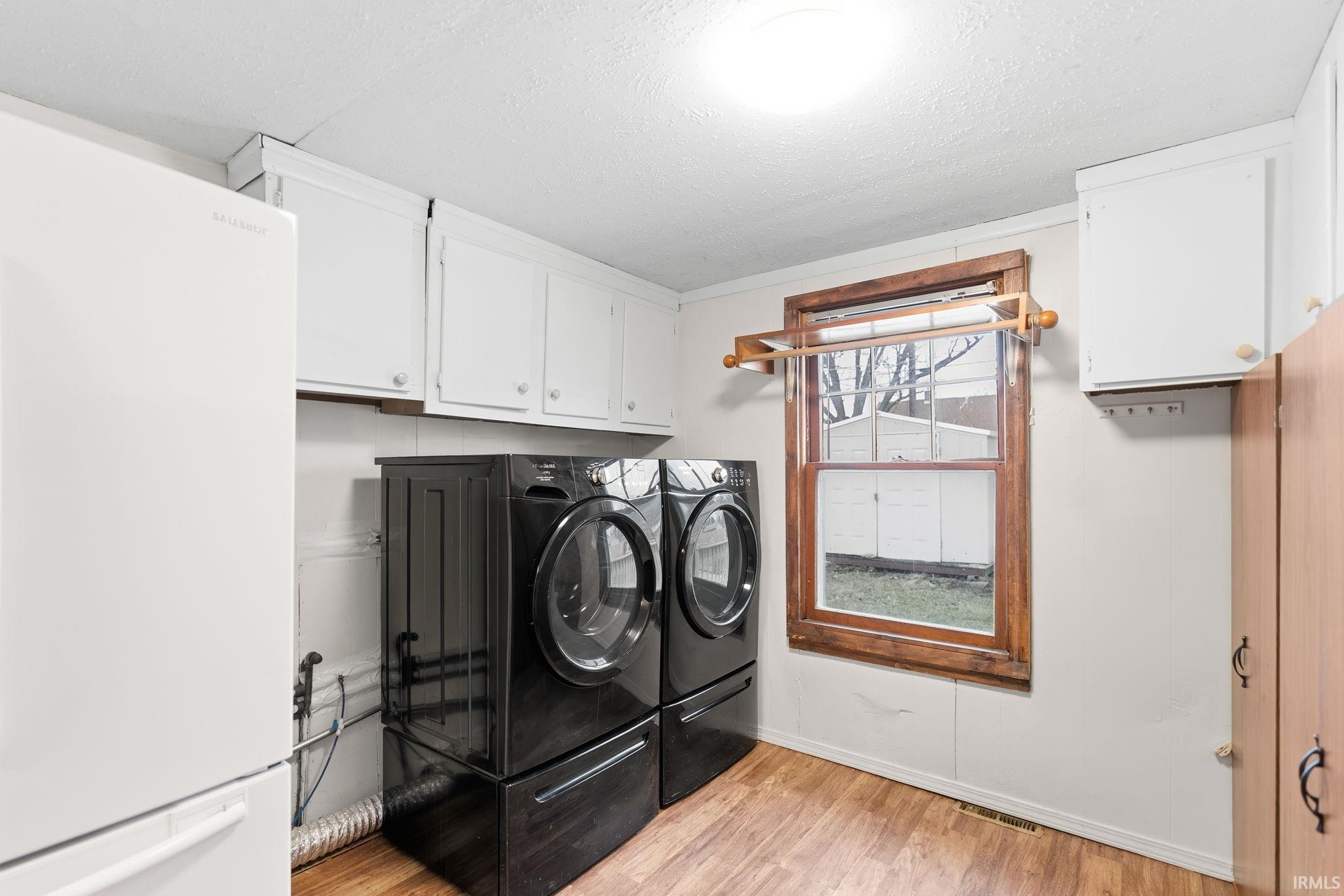 Laundry room featuring a textured ceiling, light wood finished floors, cabinet space, and separate washer and dryer