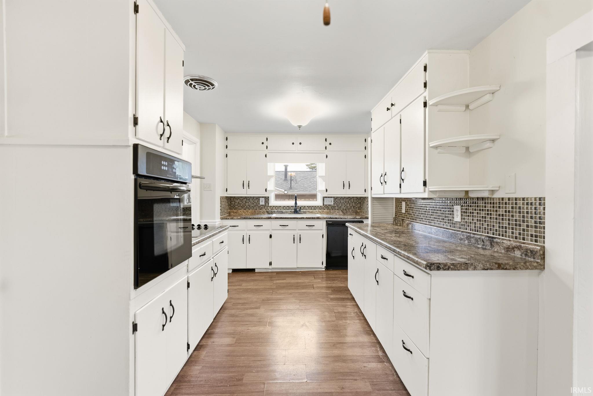 Kitchen featuring open shelves, dark countertops, black appliances, white cabinets, and light wood-style flooring