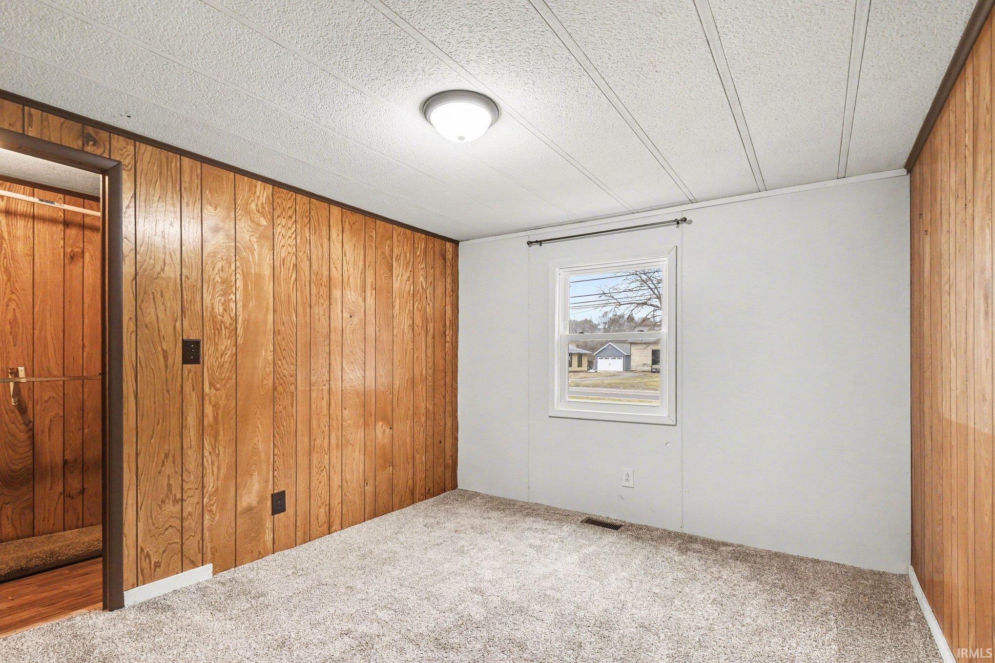 Unfurnished bedroom featuring wood walls, a closet, and carpet