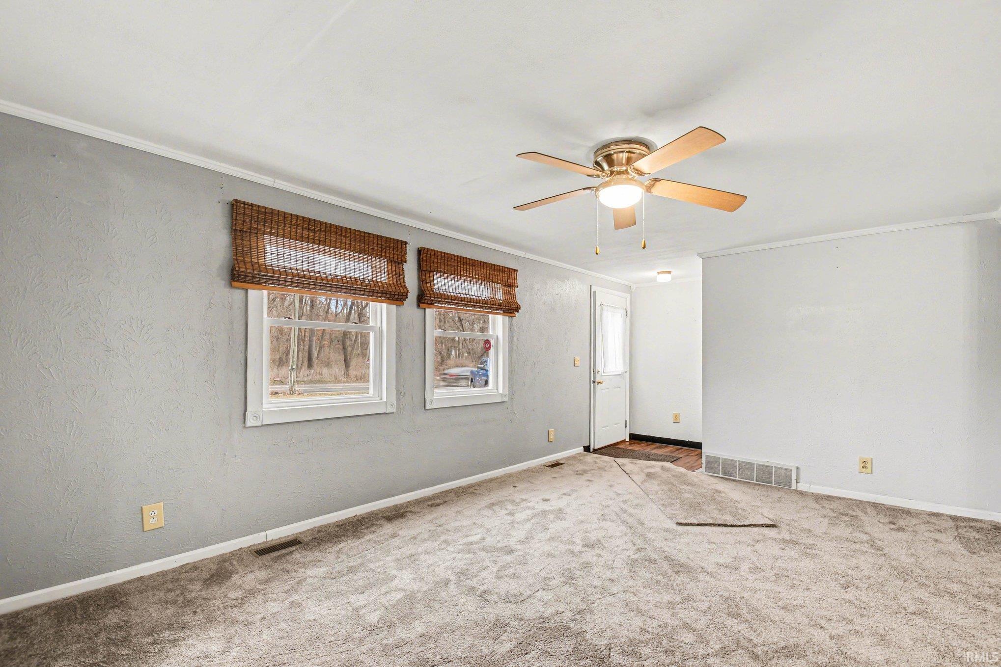 Empty room featuring carpet flooring, crown molding, and ceiling fan