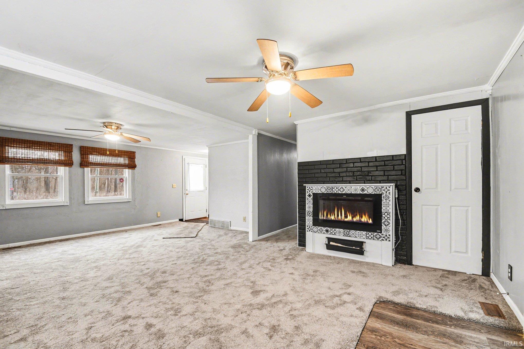 Unfurnished living room with a ceiling fan, ornamental molding, carpet, and a tiled fireplace