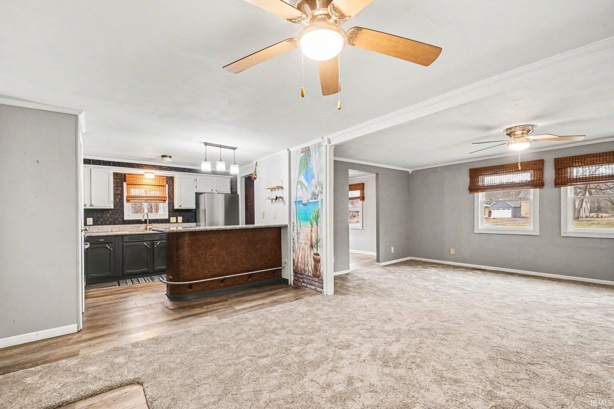 Living room with ornamental molding, ceiling fan, light carpet, and light wood-style floors