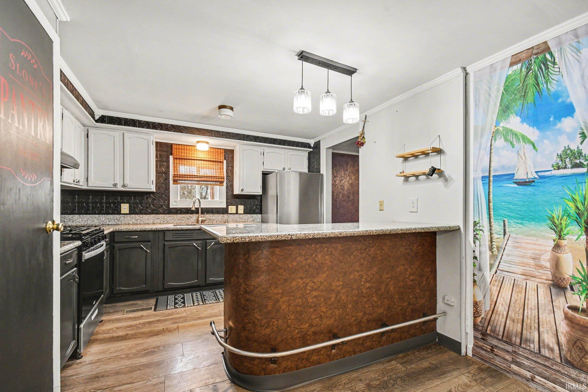 Dual tone kitchen with light wood-style floors, light stone counters, pendant lighting, freestanding refrigerator, and range with gas cooktop