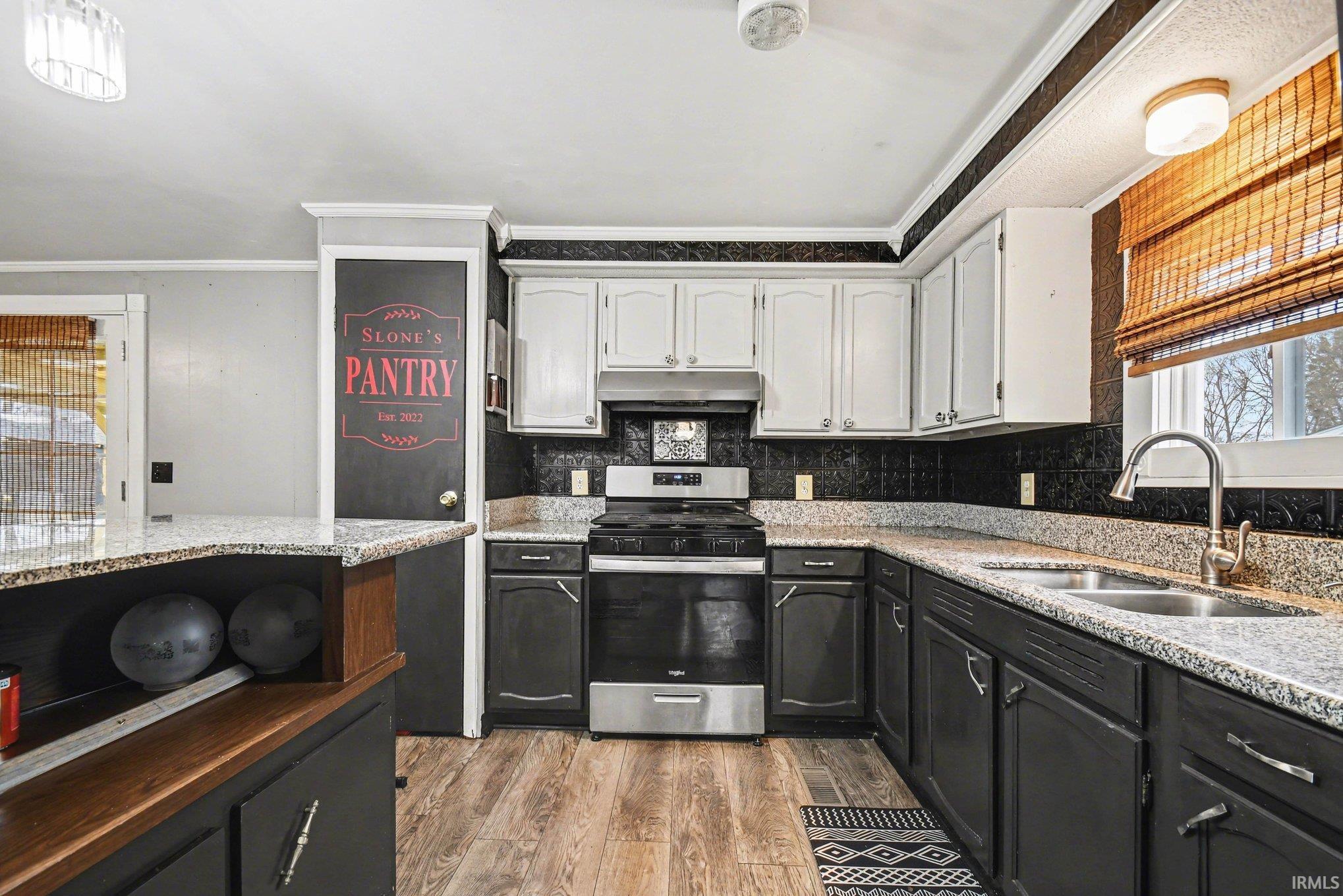 Kitchen featuring healthy amount of natural light, two tone color scheme, stainless steel range with gas stovetop, light stone counters, and light wood-style floors