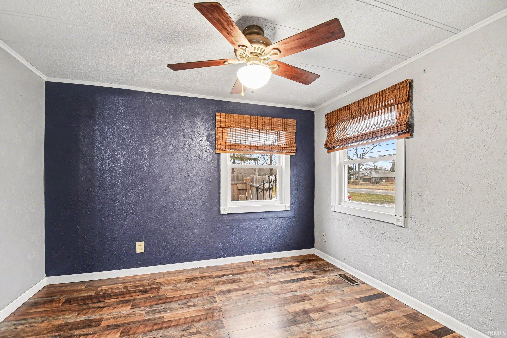 Spare room featuring ornamental molding, a textured wall, wood finished floors, a textured ceiling, and ceiling fan