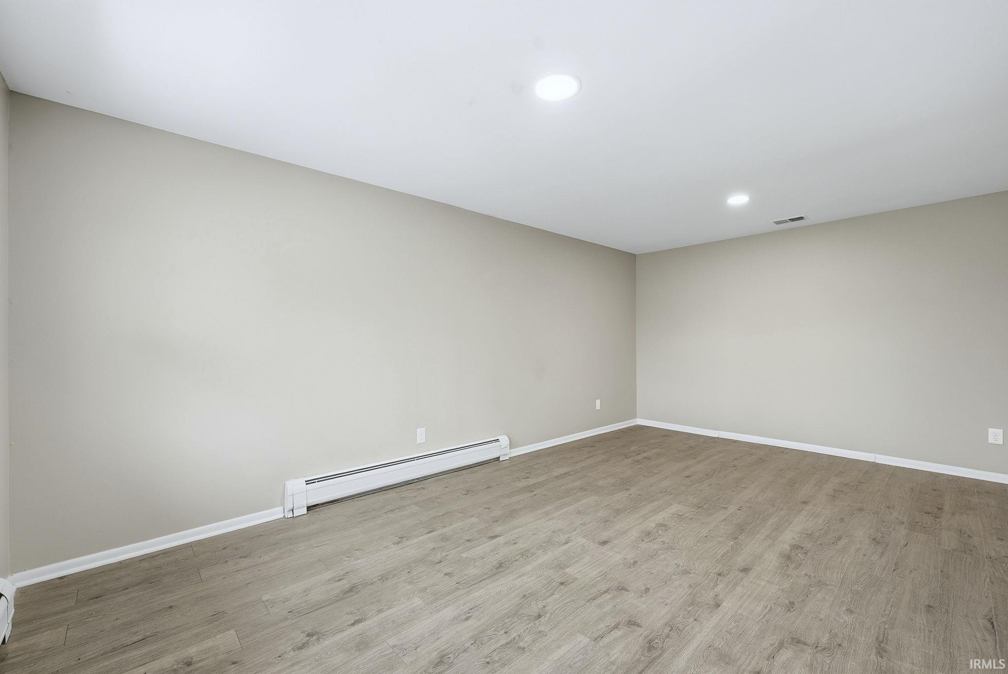 Unfurnished room featuring a baseboard radiator, light wood-style flooring, and recessed lighting