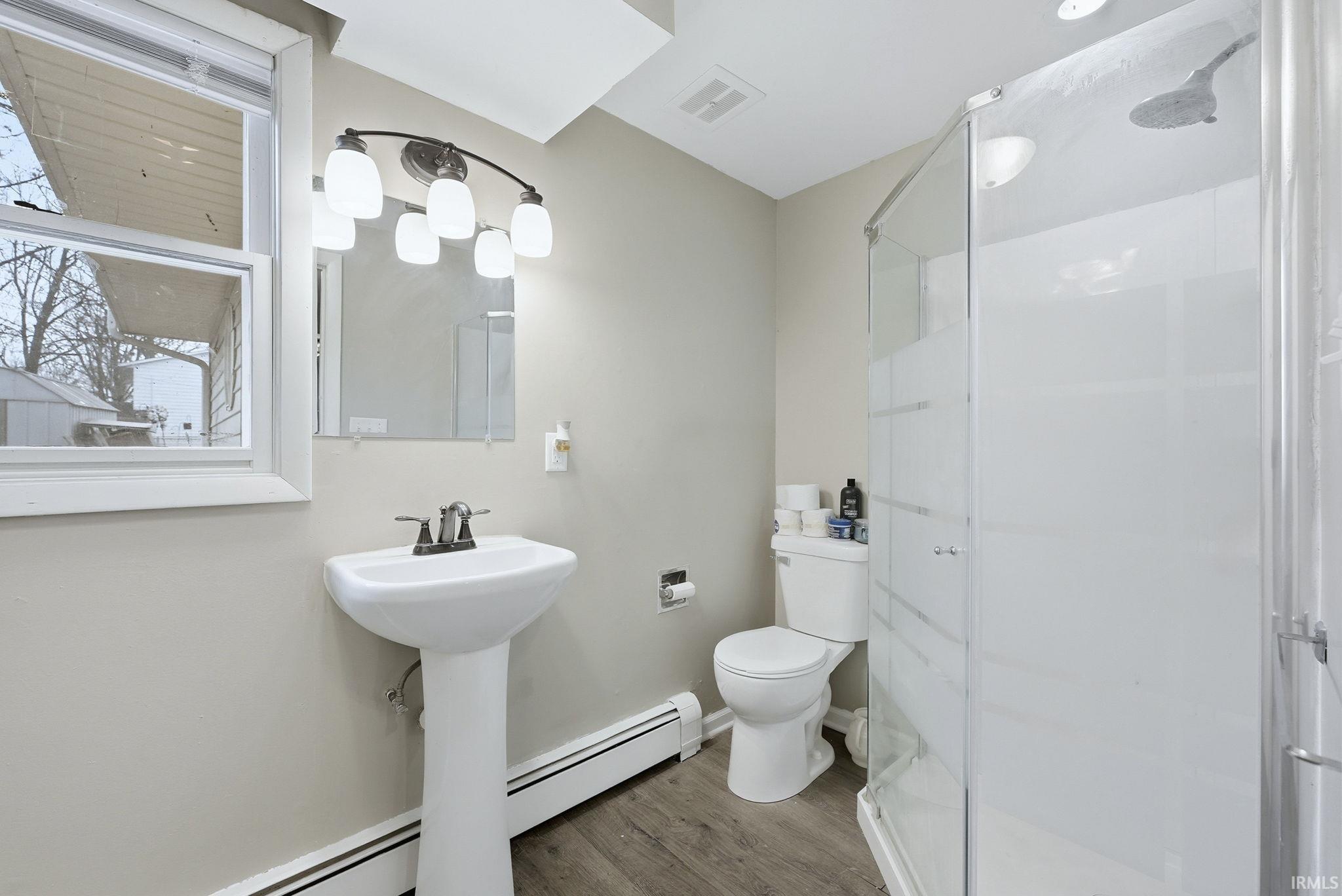 Full bathroom featuring a stall shower, wood finished floors, and a baseboard heating unit