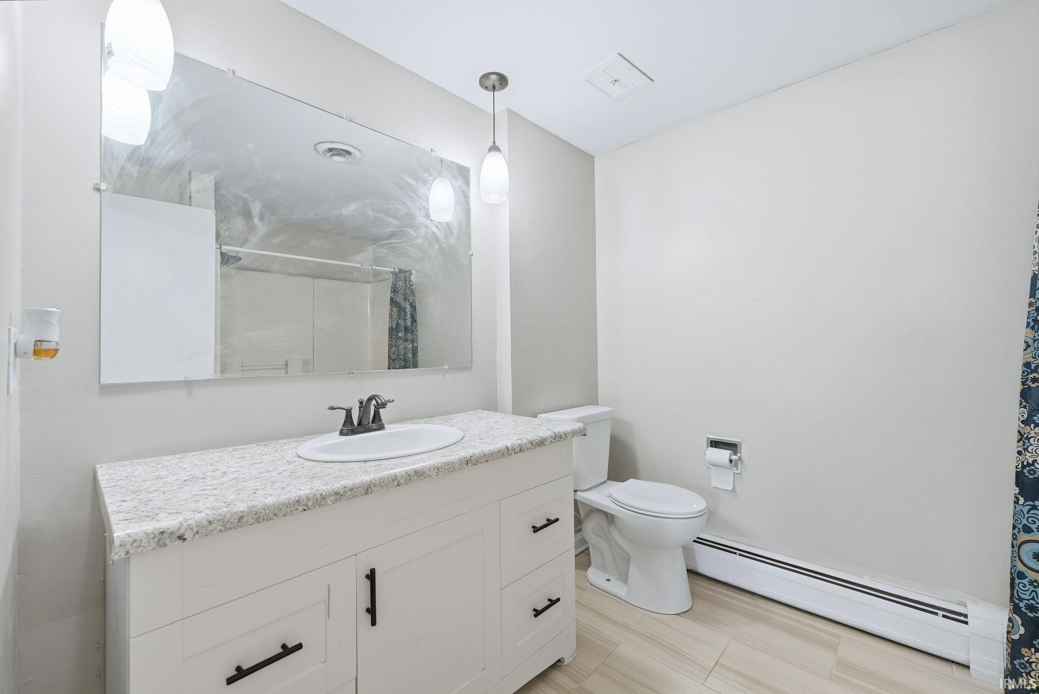 Bathroom featuring a baseboard heating unit, vanity, and curtained shower