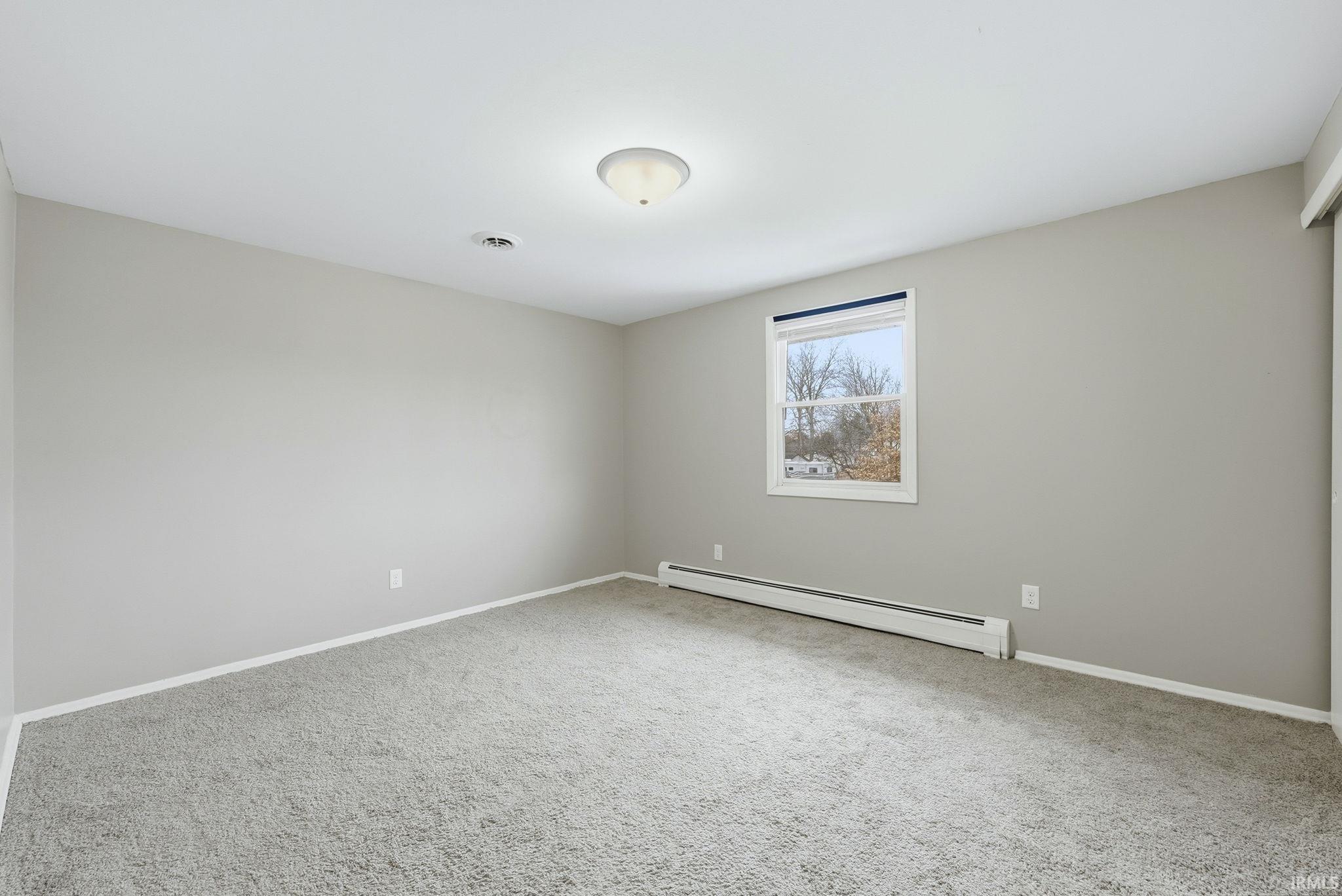 Carpeted spare room with a baseboard radiator and baseboards