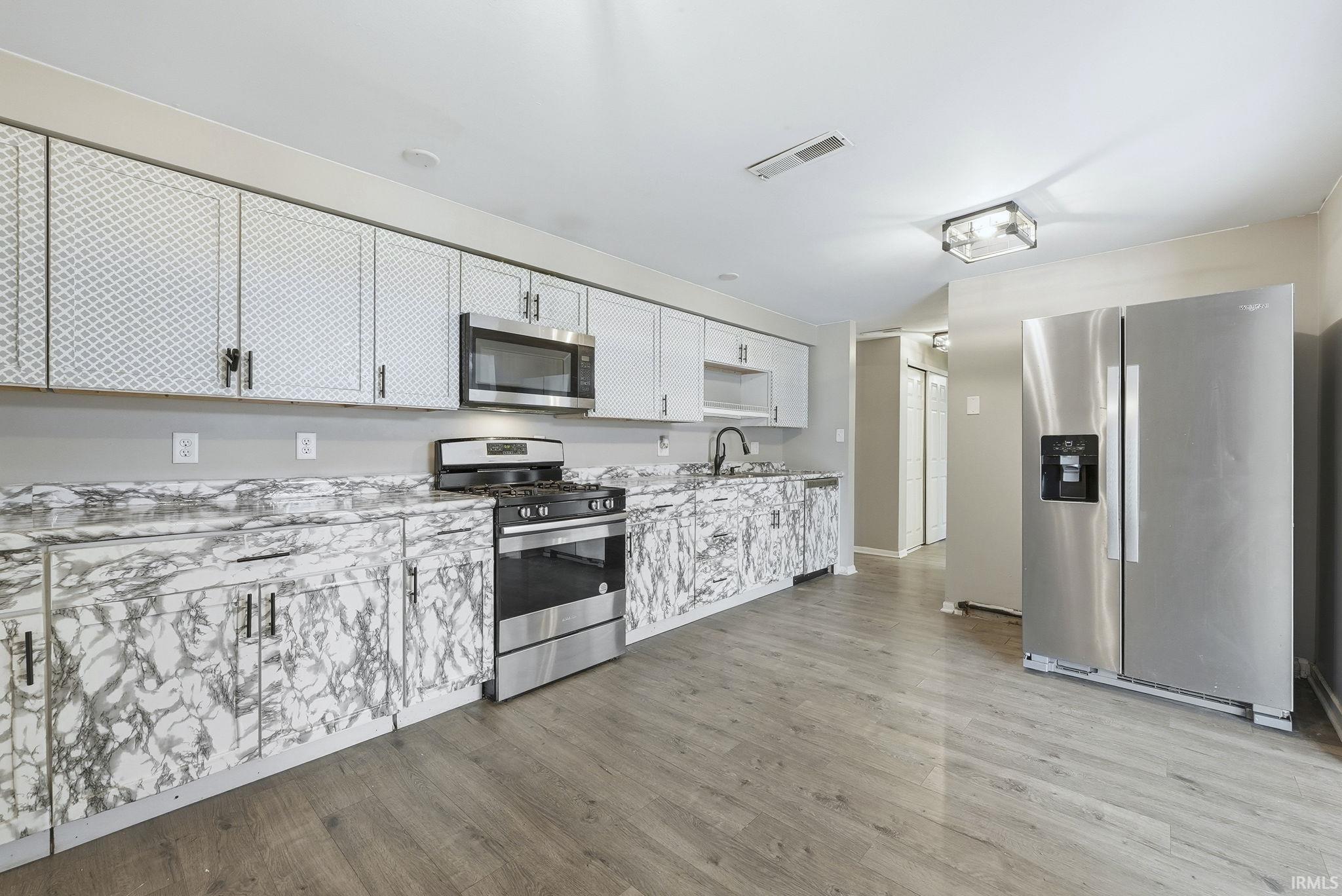 Kitchen with stainless steel appliances, light wood-type flooring, white cabinetry, and open shelves