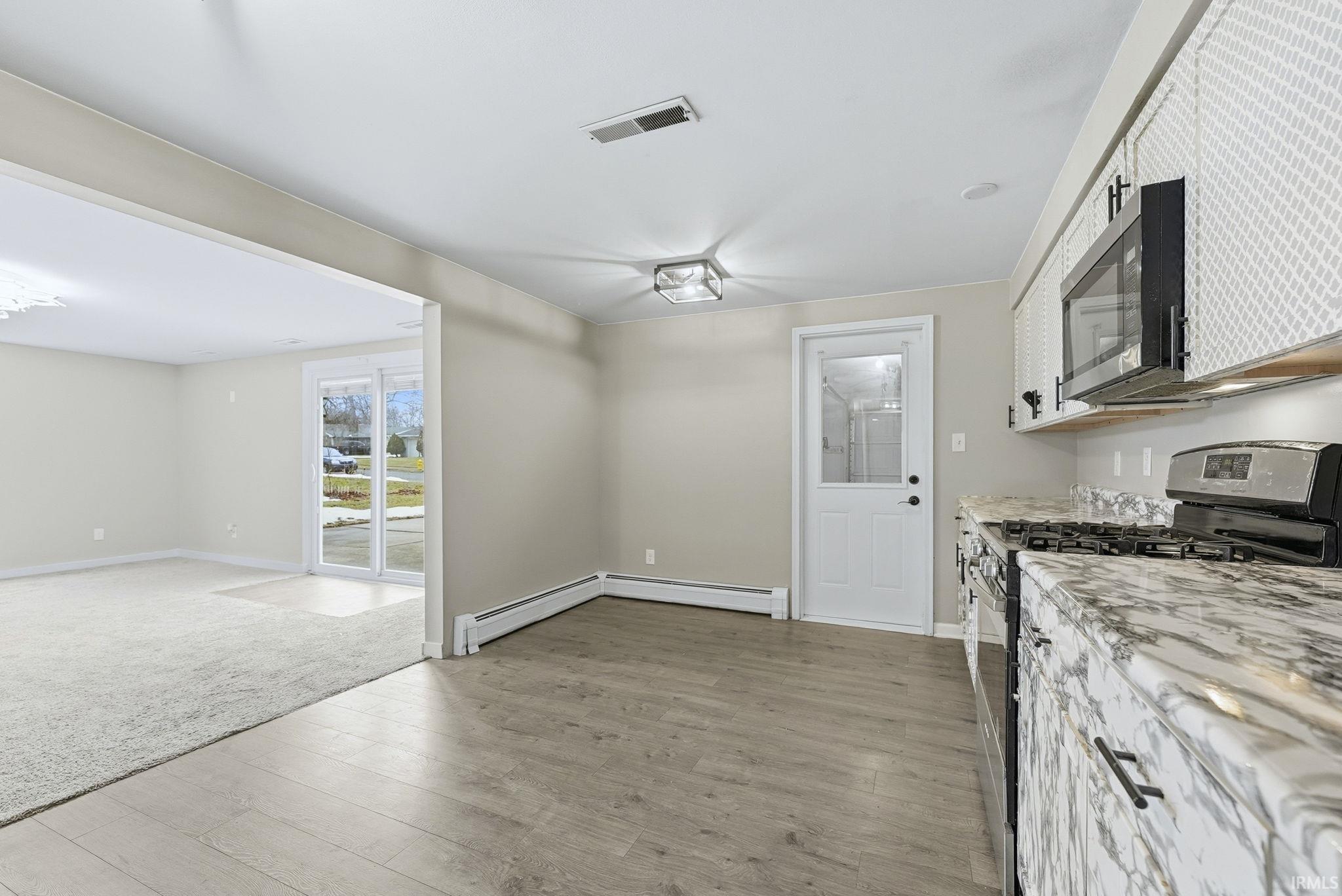 Kitchen with stainless steel appliances, light wood-type flooring, light stone counters, white cabinets, and a baseboard heating unit