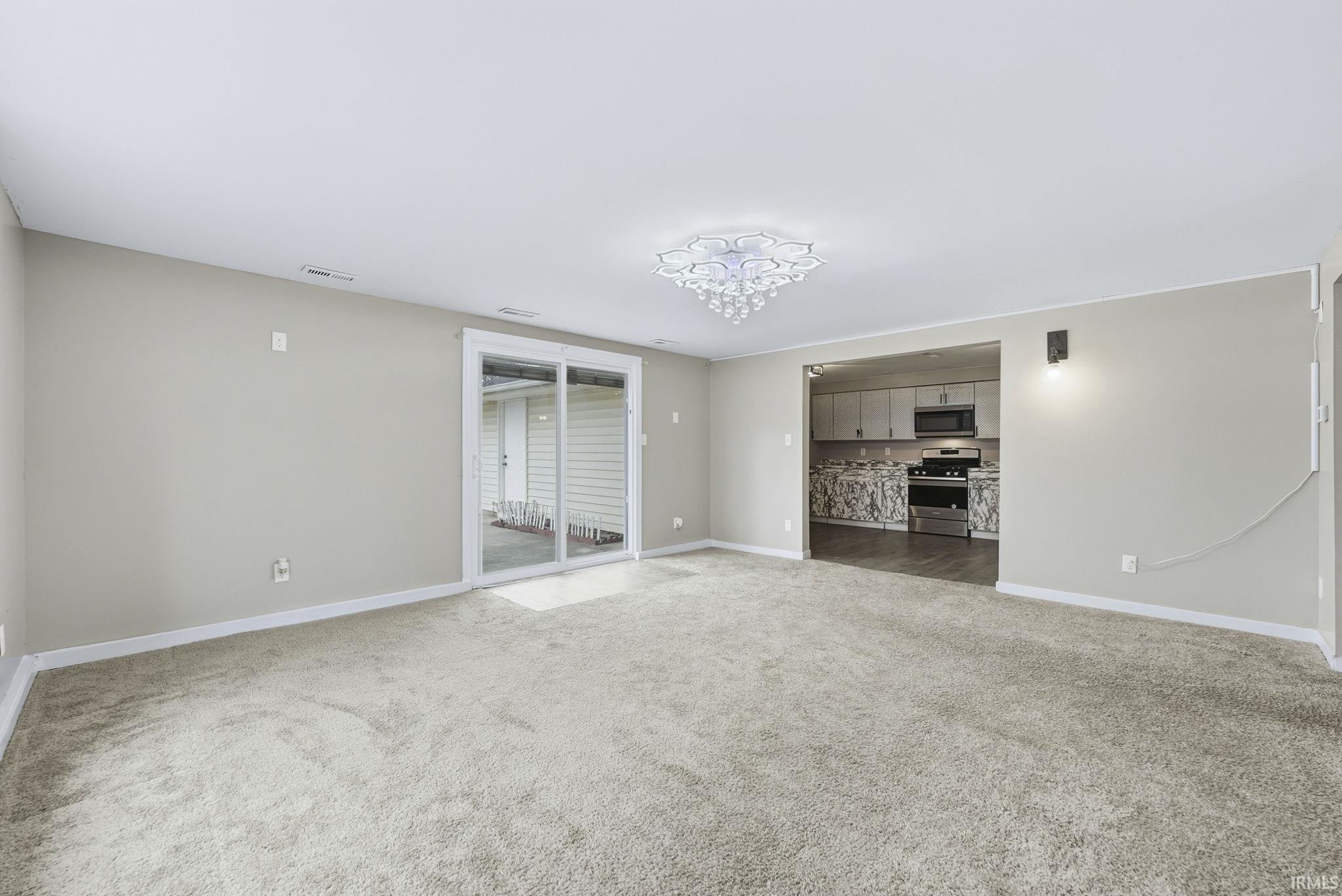 Unfurnished living room featuring light colored carpet and a chandelier