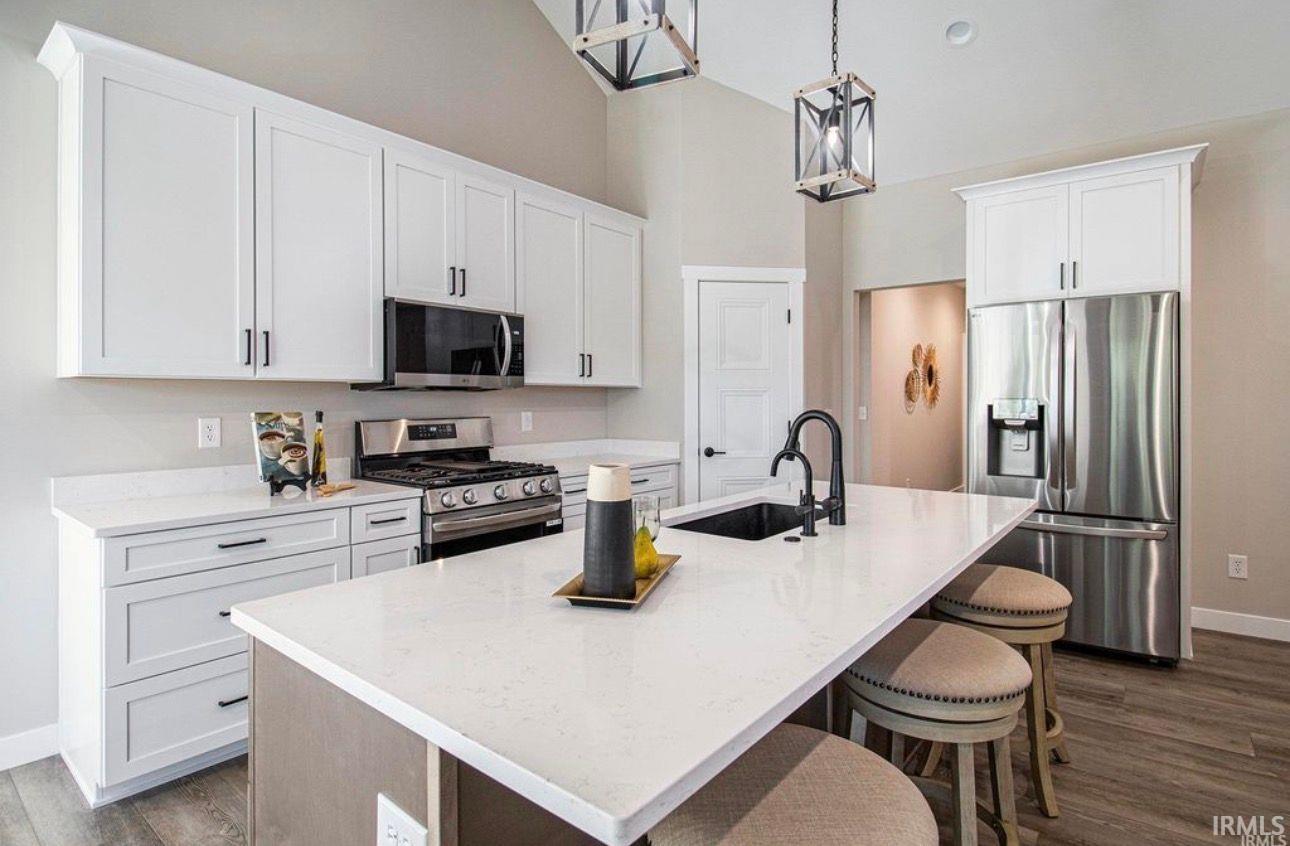 Kitchen with stainless steel appliances, a kitchen island with sink, dark wood finished floors, a kitchen breakfast bar, and a high ceiling