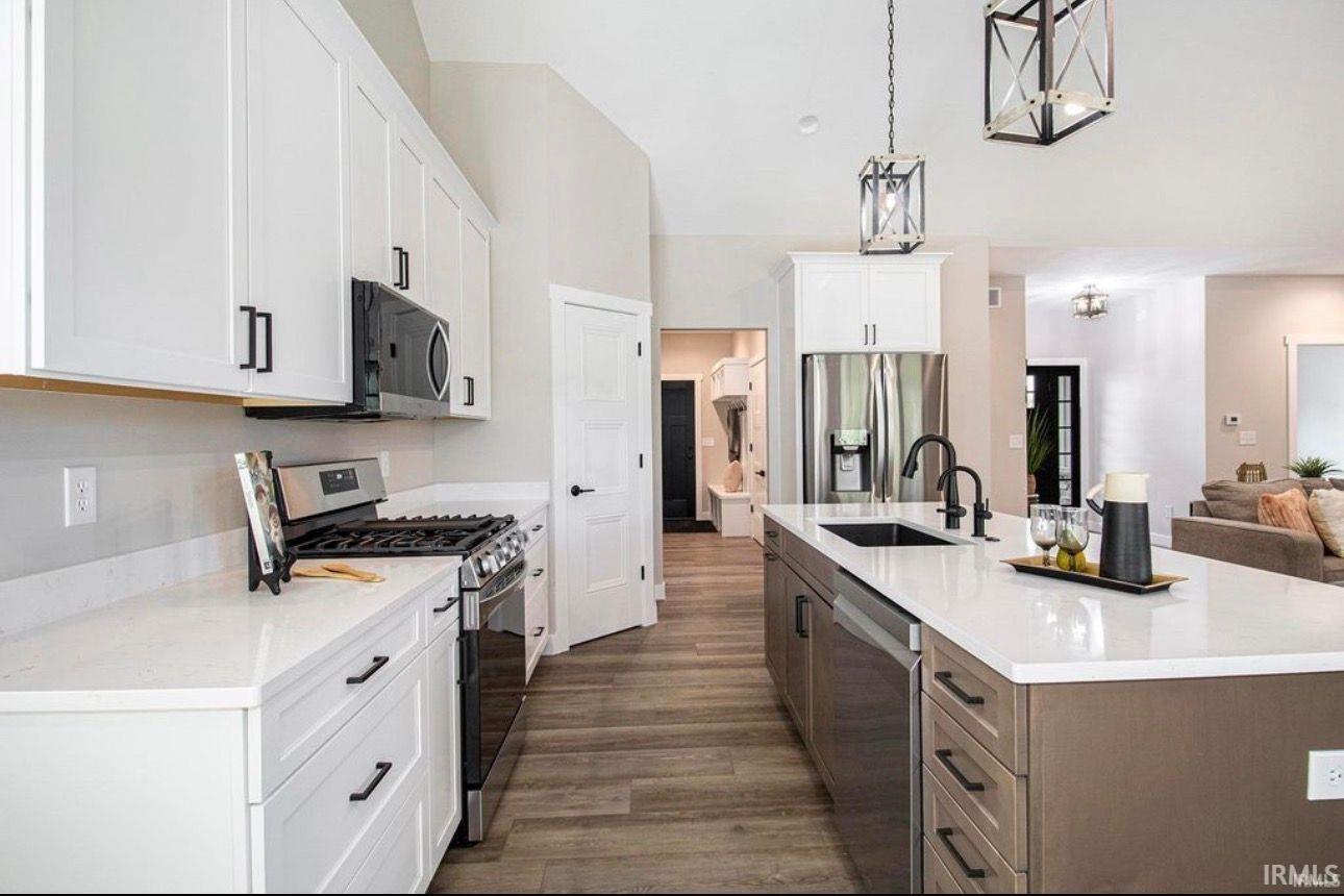 Dual tone kitchen featuring dual tone cabinets, stainless steel appliances, an island with sink, decorative light fixtures, and open floor plan