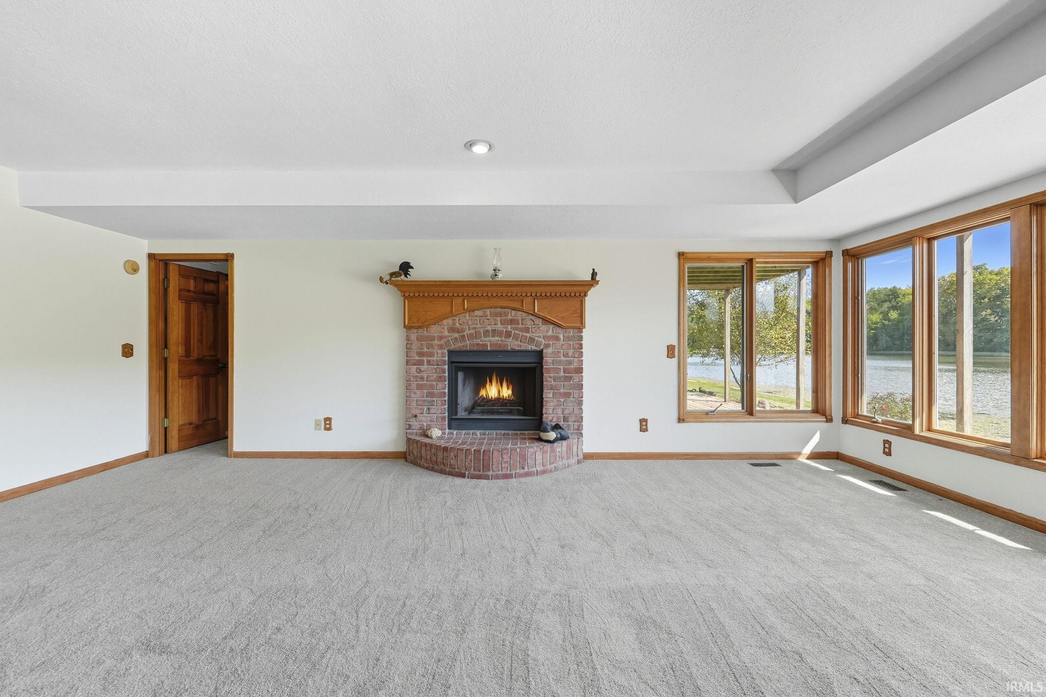 Unfurnished living room featuring carpet floors, a brick fireplace, a water view, and recessed lighting