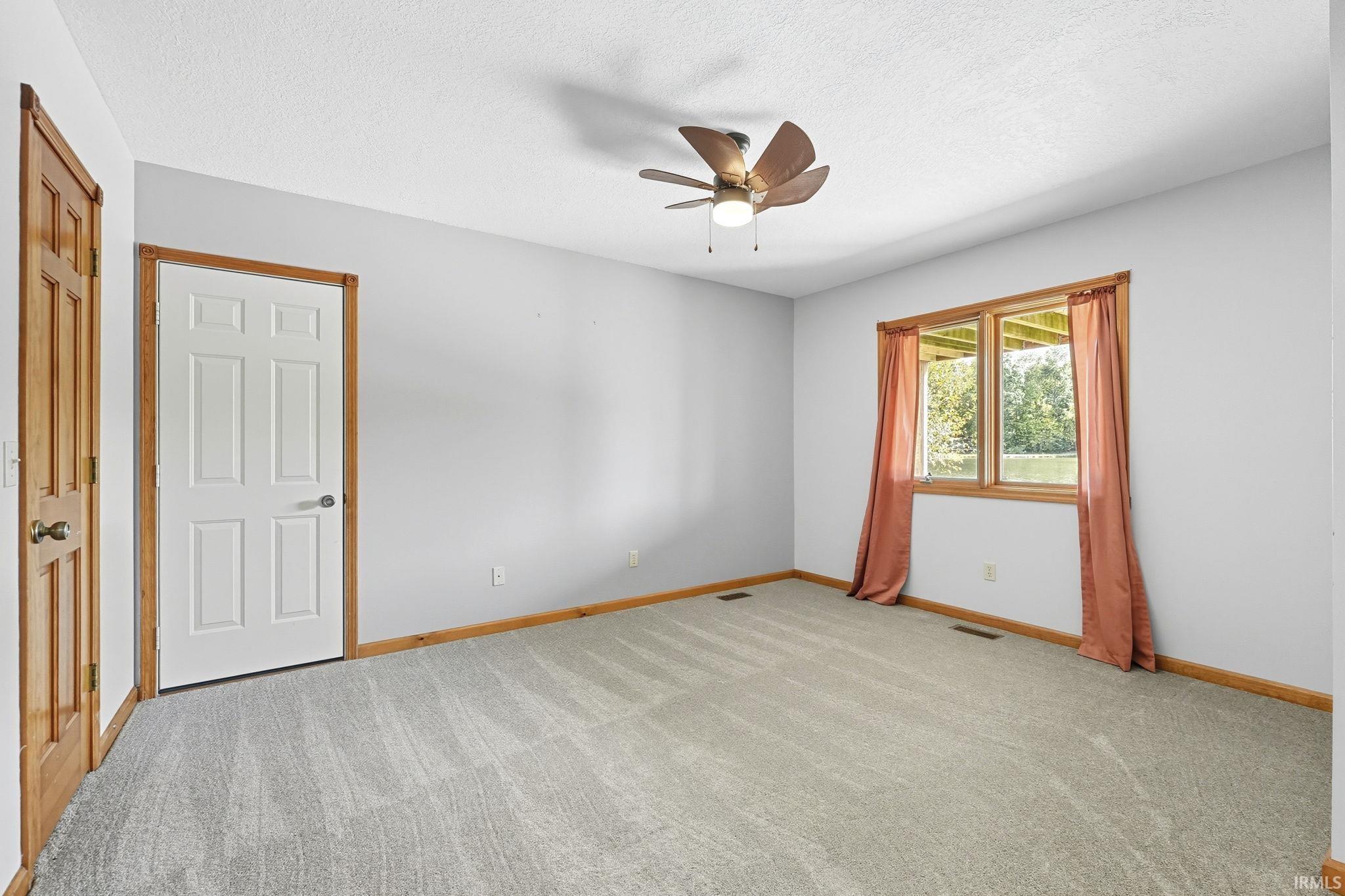Empty room with light carpet, ceiling fan, and a textured ceiling