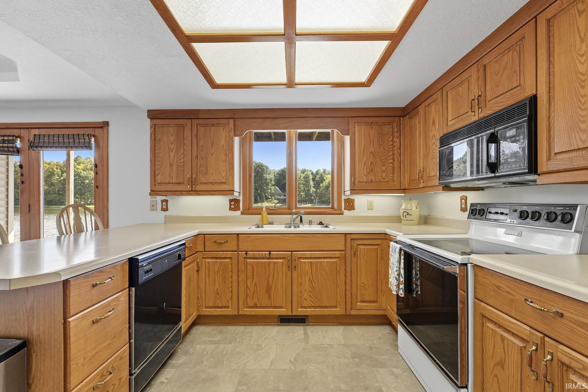 Kitchen with black appliances, wood finish cabinetry, light countertops, and healthy amount of natural light