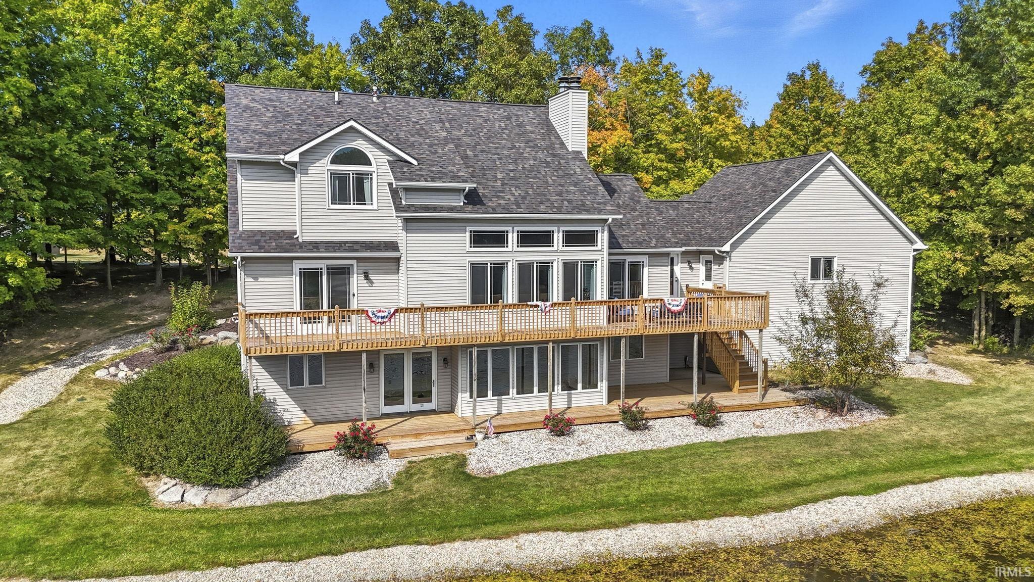 Back of house featuring a wooden deck, a chimney, a lawn, and a shingled roof