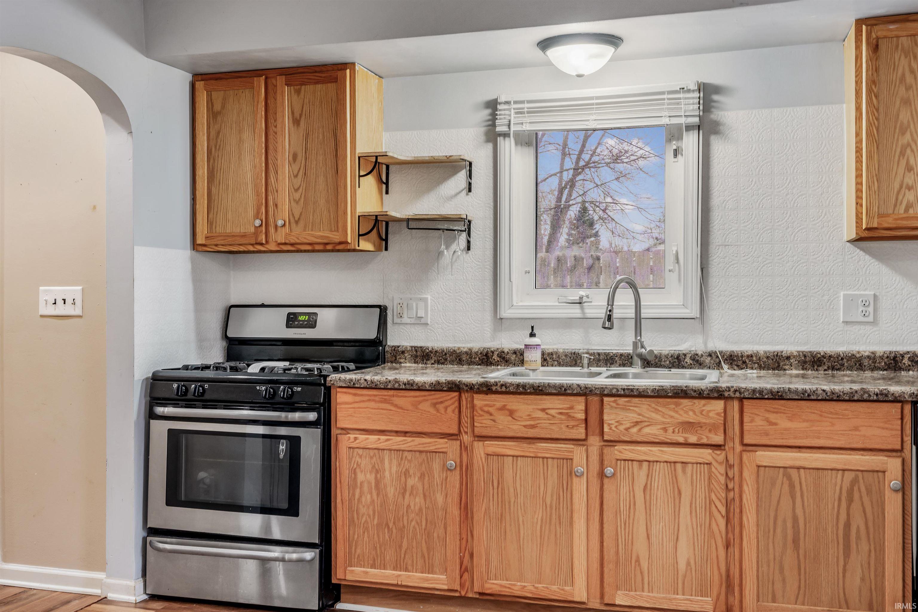 Kitchen featuring stainless steel range with gas stovetop, open shelves, dark countertops, arched walkways, and a textured wall