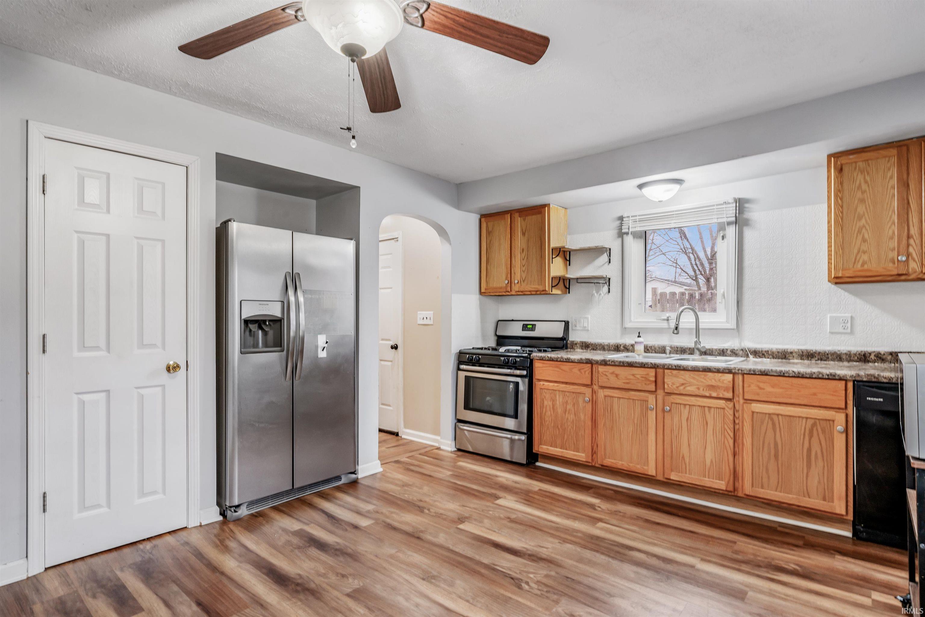 Kitchen featuring stainless steel appliances, a ceiling fan, arched walkways, light wood-style flooring, and open shelves