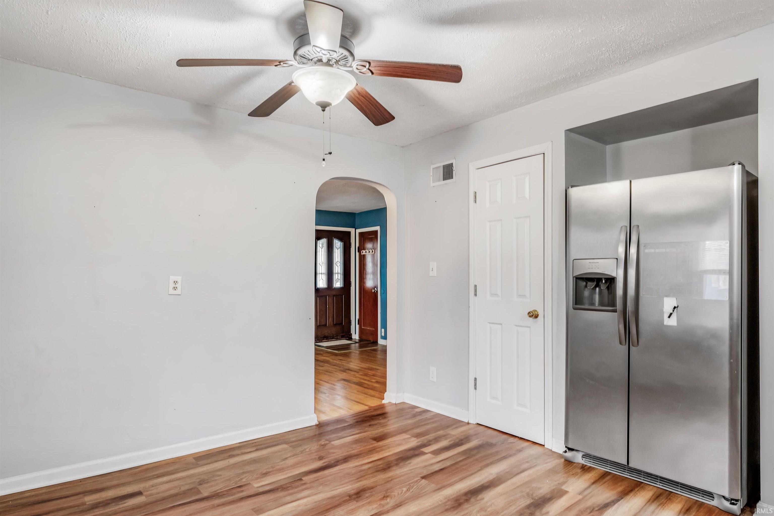 Kitchen featuring stainless steel refrigerator with ice dispenser, arched walkways, light wood-style flooring, ceiling fan, and a textured ceiling