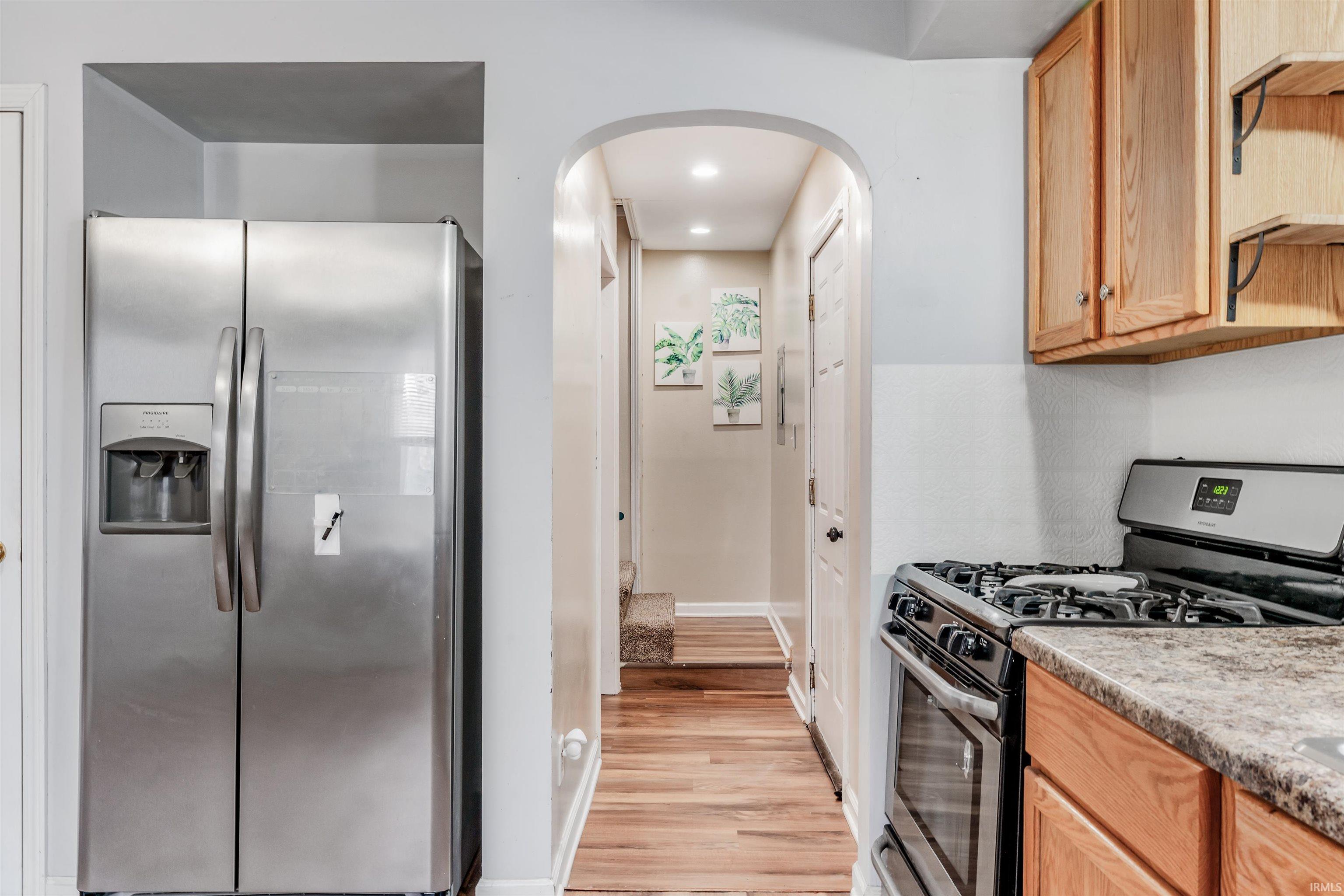 Kitchen with stainless steel appliances, arched walkways, light wood-style floors, recessed lighting, and light wood finish cabinetry