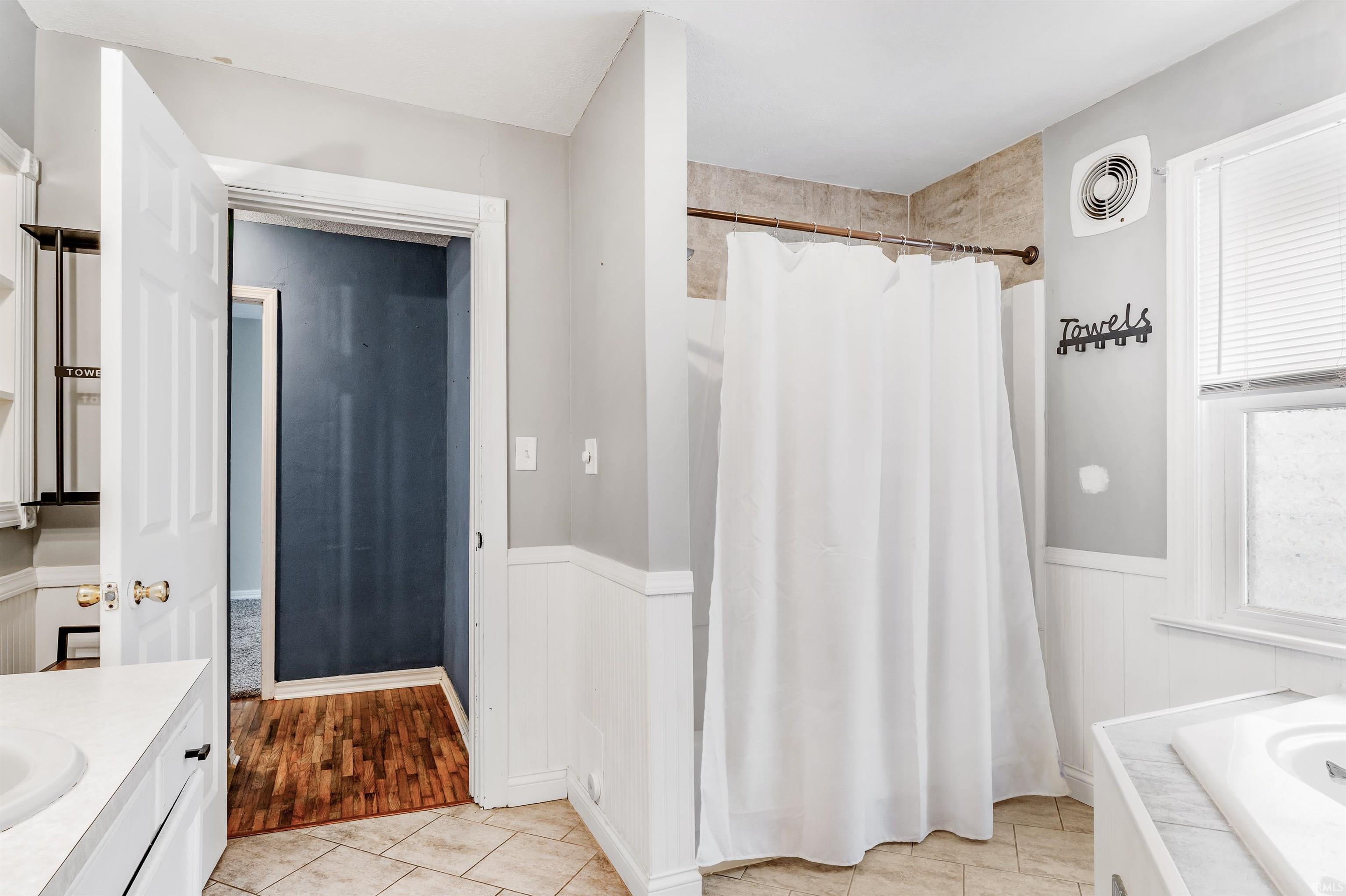 Bathroom featuring vanity, a shower with shower curtain, light tile patterned floors, and wainscoting