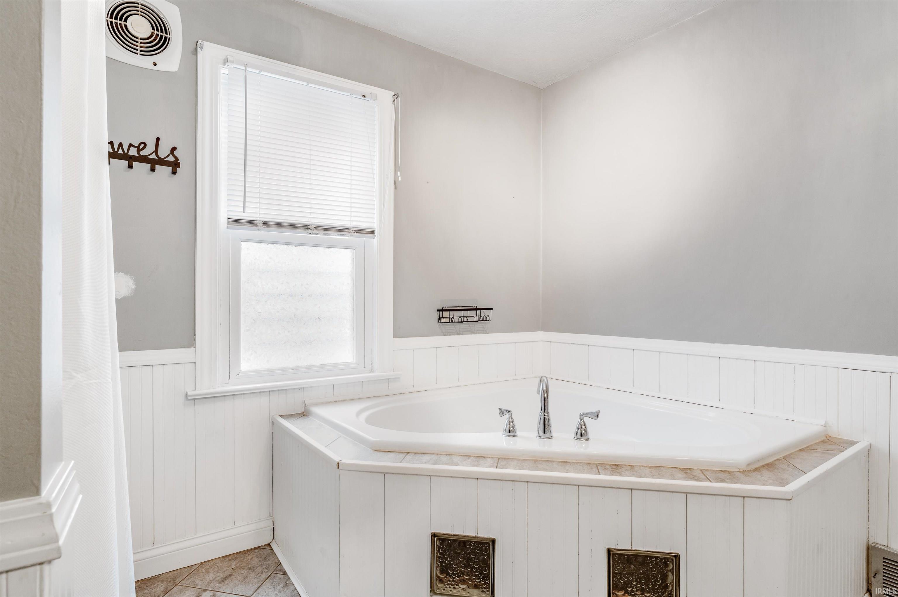 Bathroom with a wainscoted wall, a bath, and light tile patterned floors