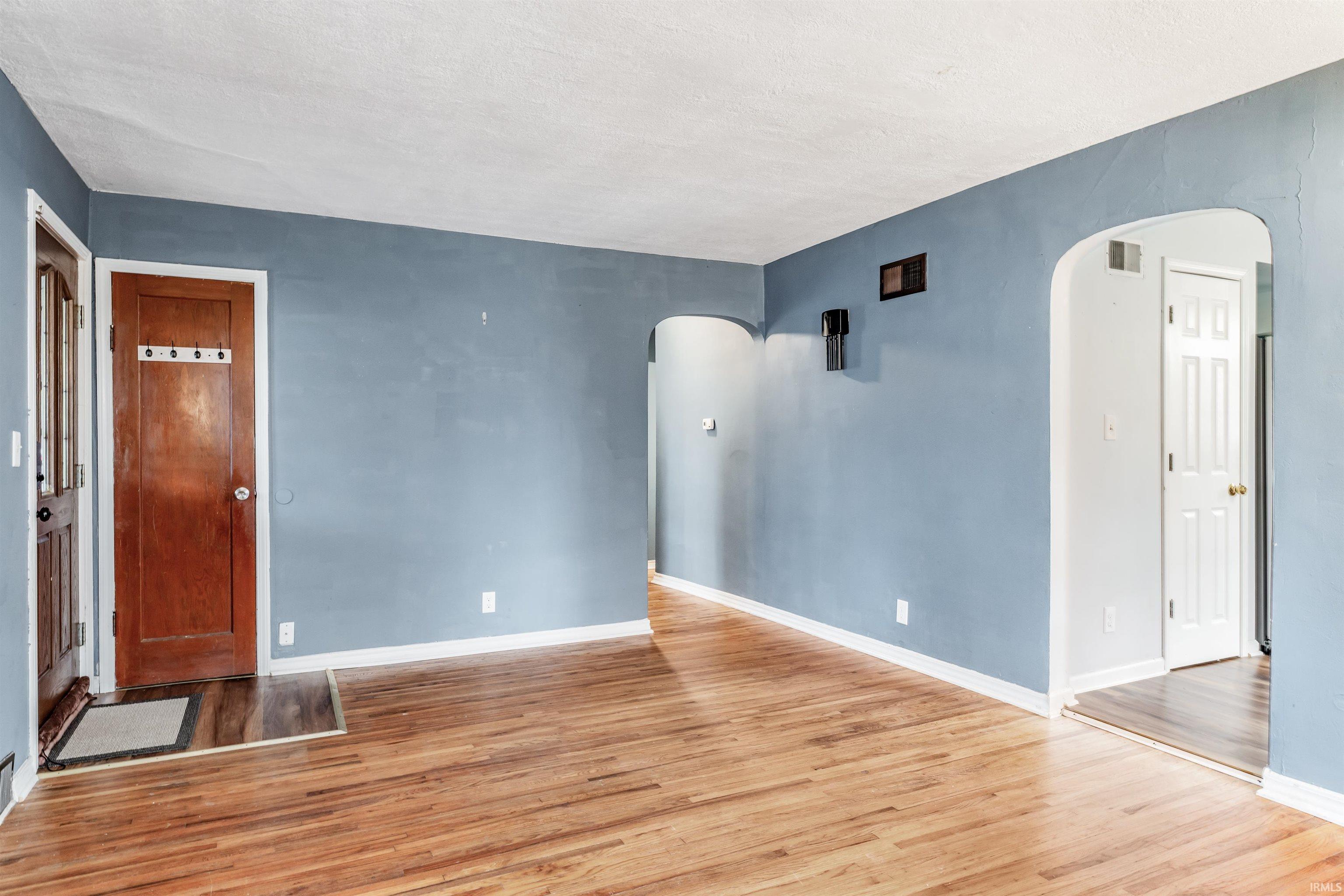 Unfurnished living room with arched walkways and light wood-type flooring