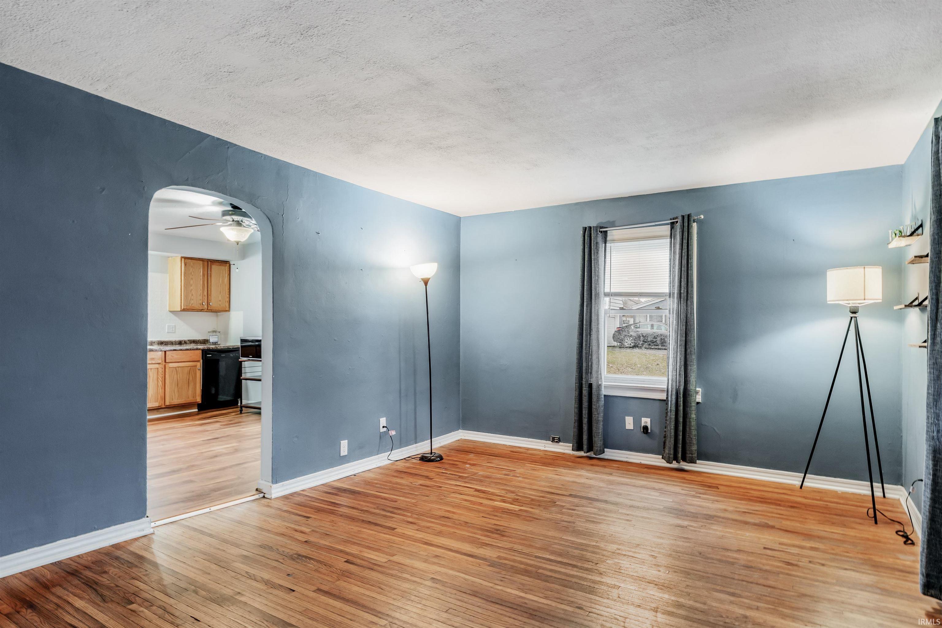Empty room with light wood finished floors, a ceiling fan, arched walkways, and a textured ceiling