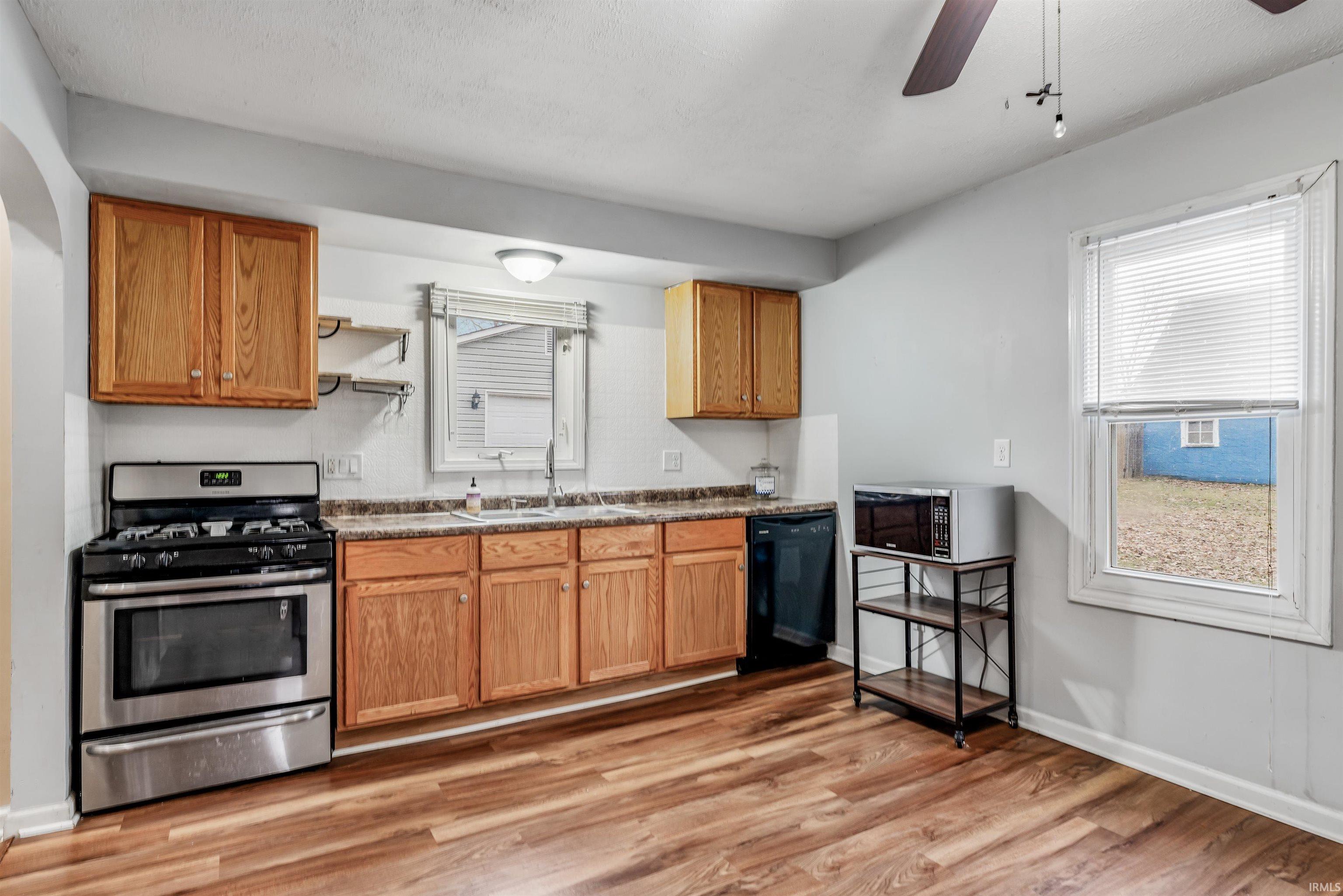Kitchen with stainless steel gas stove, ceiling fan, light wood-style flooring, and black dishwasher