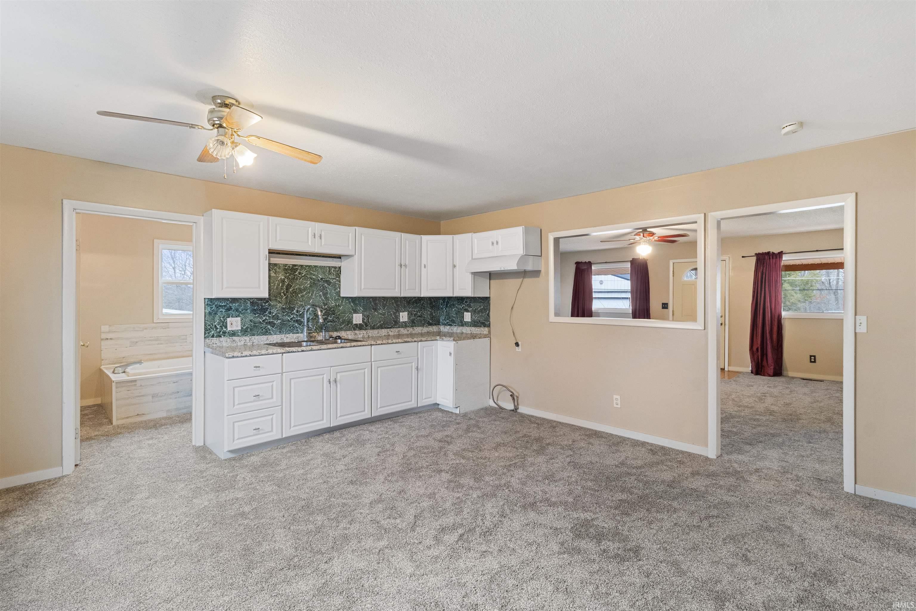 Kitchen with a ceiling fan, white cabinets, tasteful backsplash, and light carpet