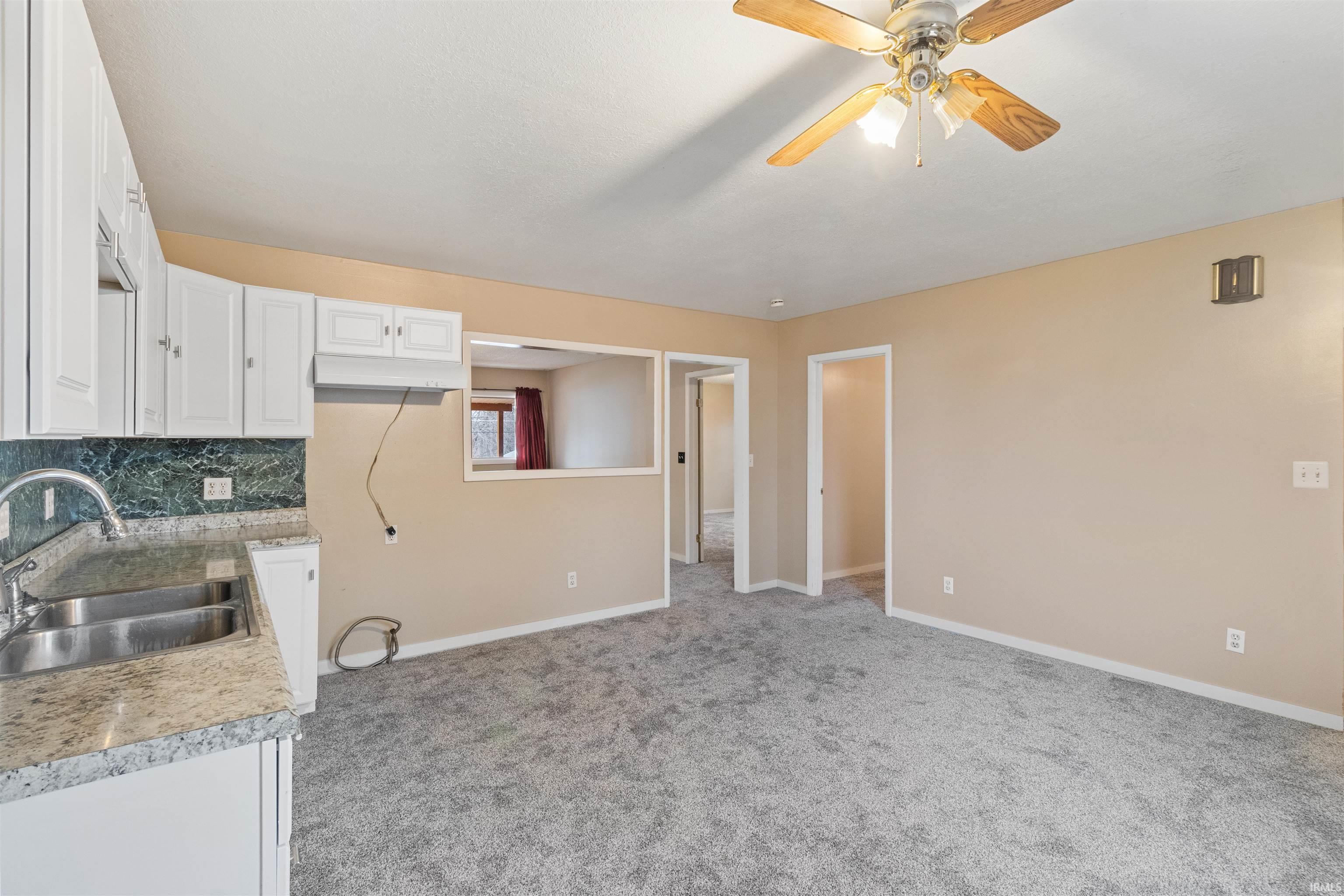 Kitchen featuring white cabinets, light colored carpet, light countertops, decorative backsplash, and a ceiling fan
