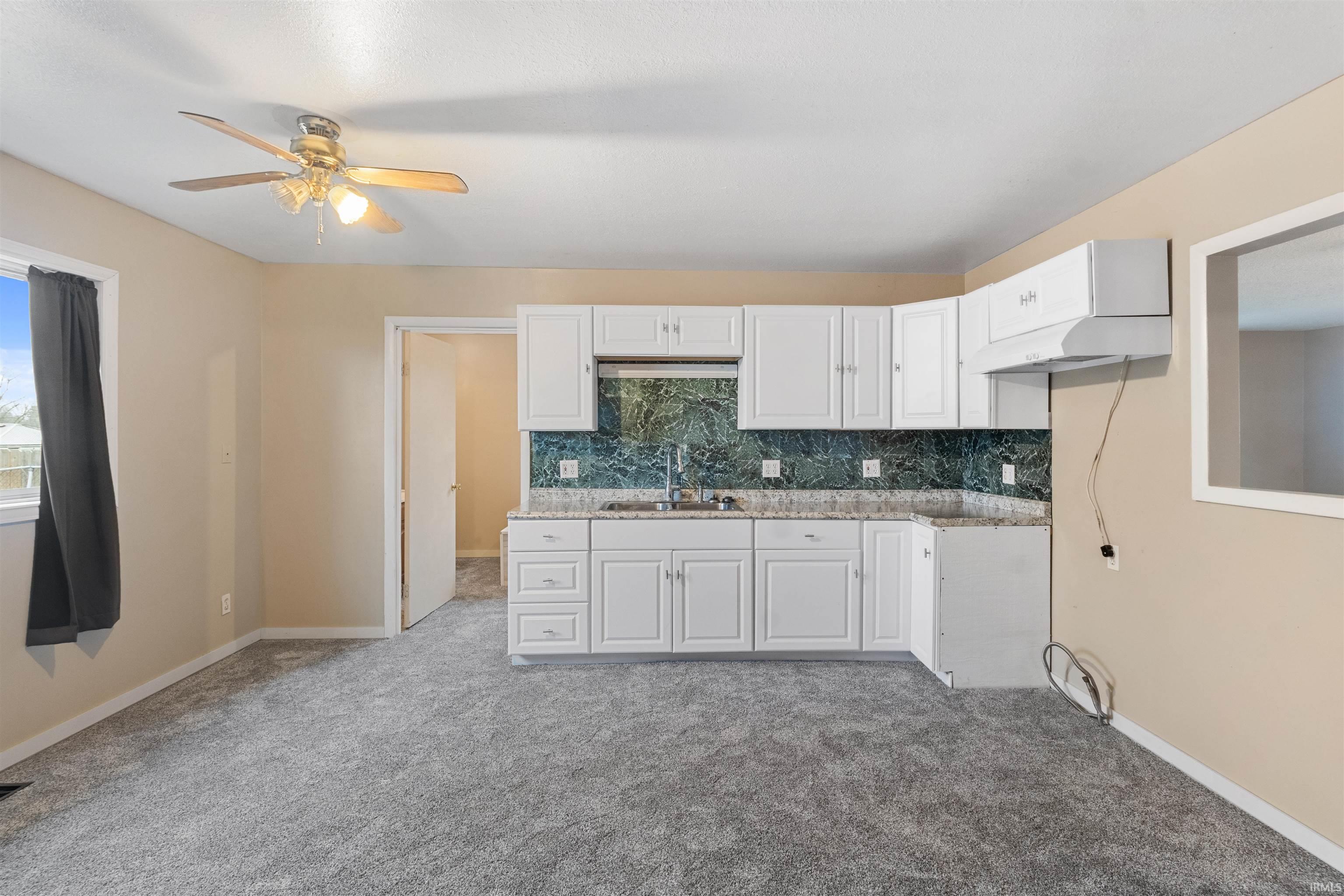 Kitchen with tasteful backsplash, white cabinetry, light carpet, a ceiling fan, and light stone counters