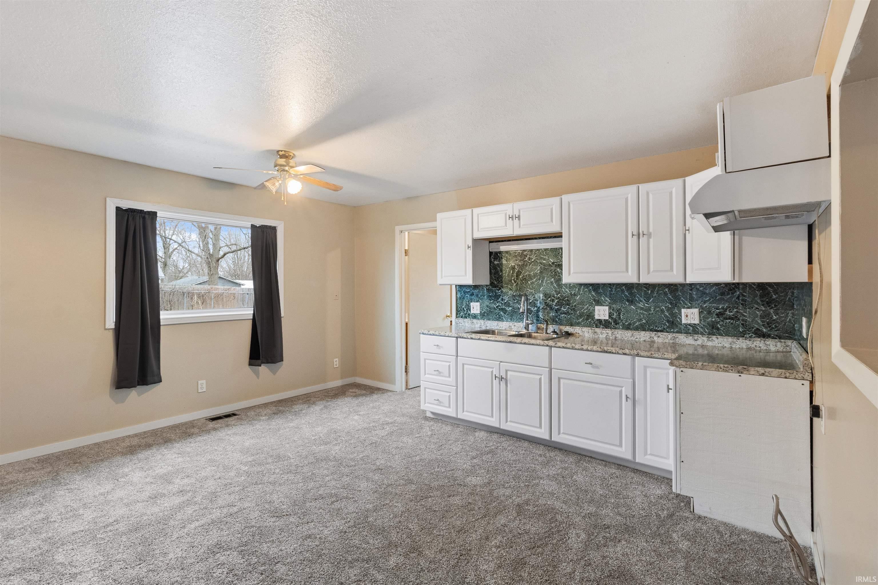Kitchen featuring backsplash, white cabinetry, a ceiling fan, light colored carpet, and light stone counters