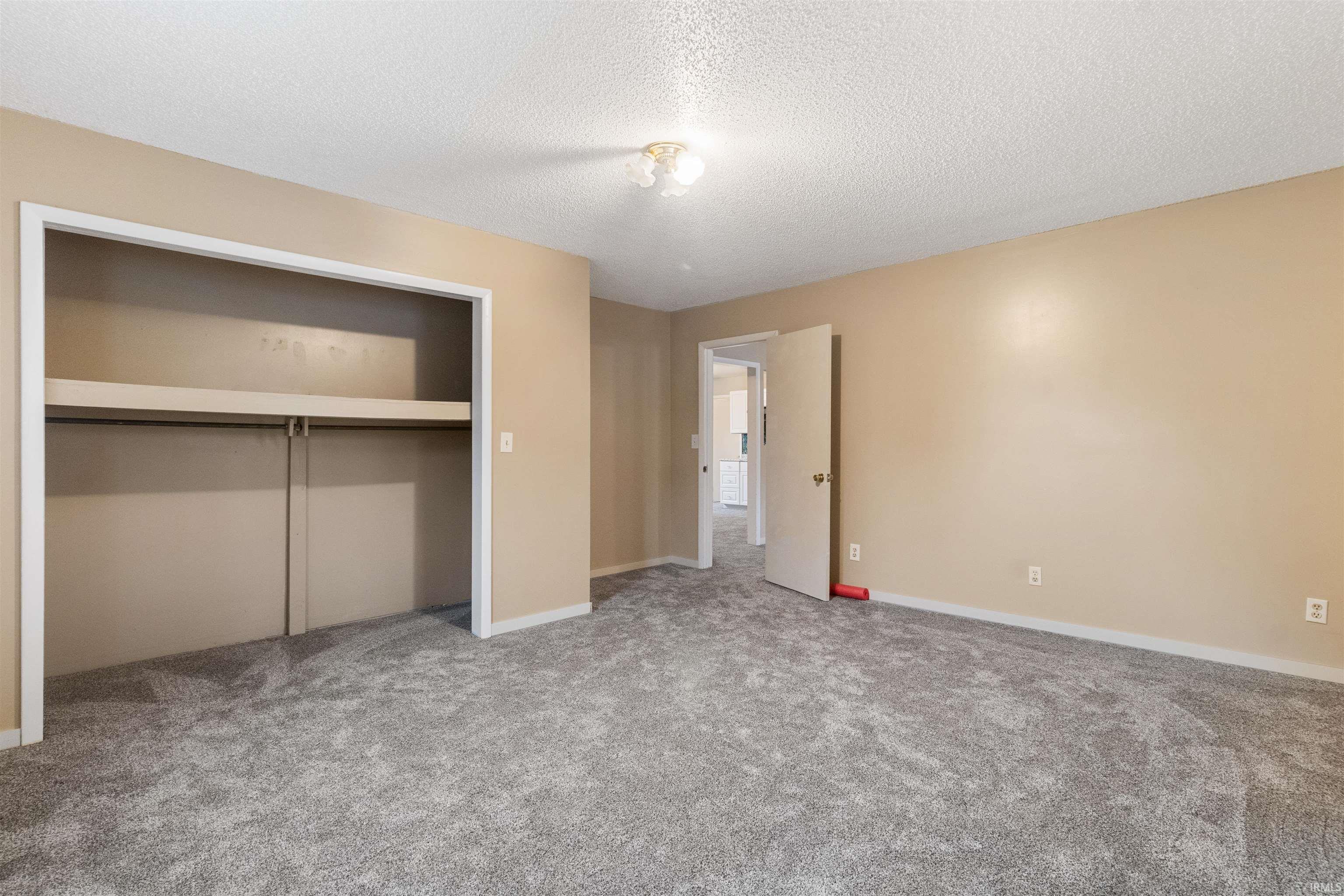 Unfurnished bedroom featuring a closet, light carpet, and a textured ceiling
