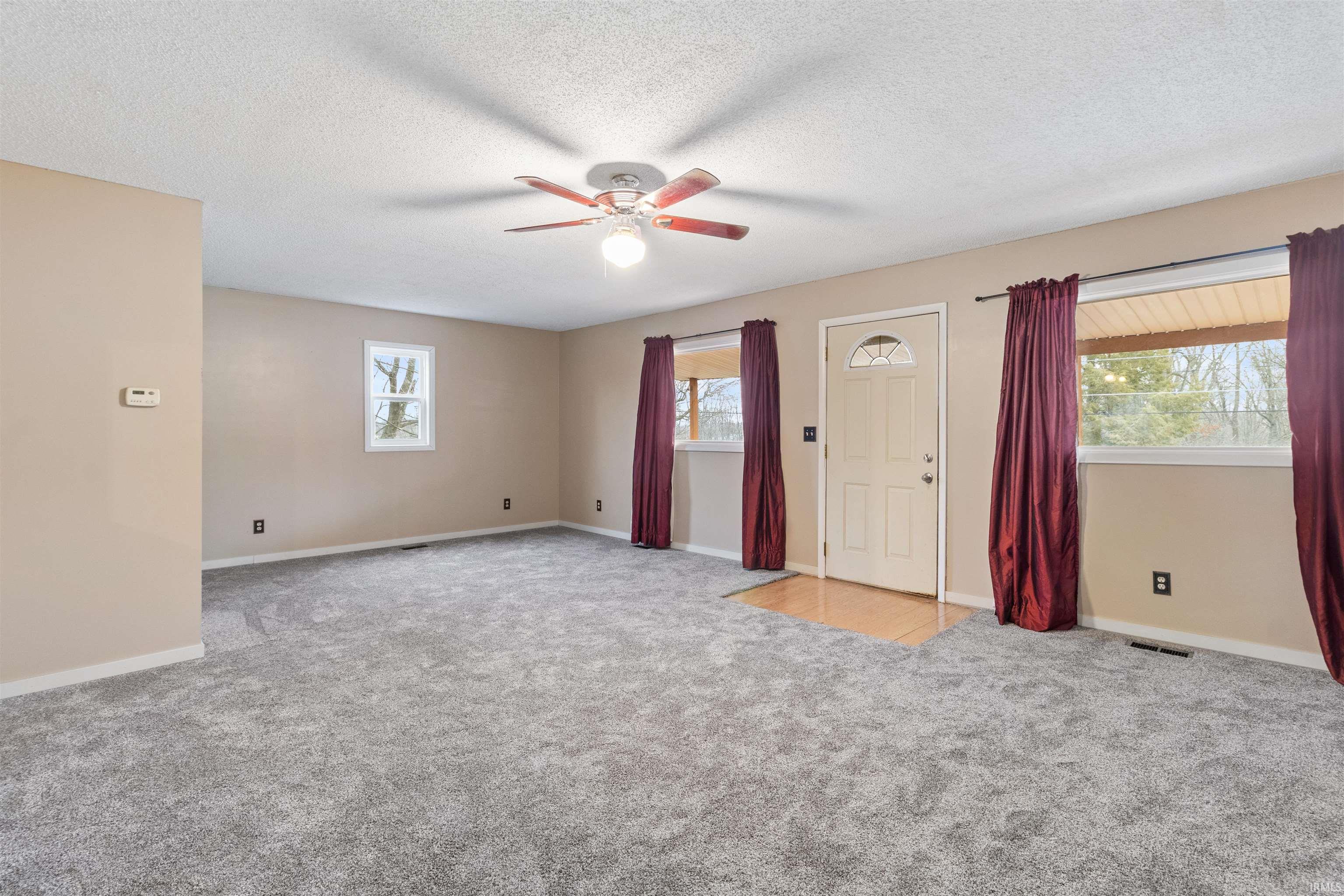 Unfurnished living room with light colored carpet, a textured ceiling, and a ceiling fan